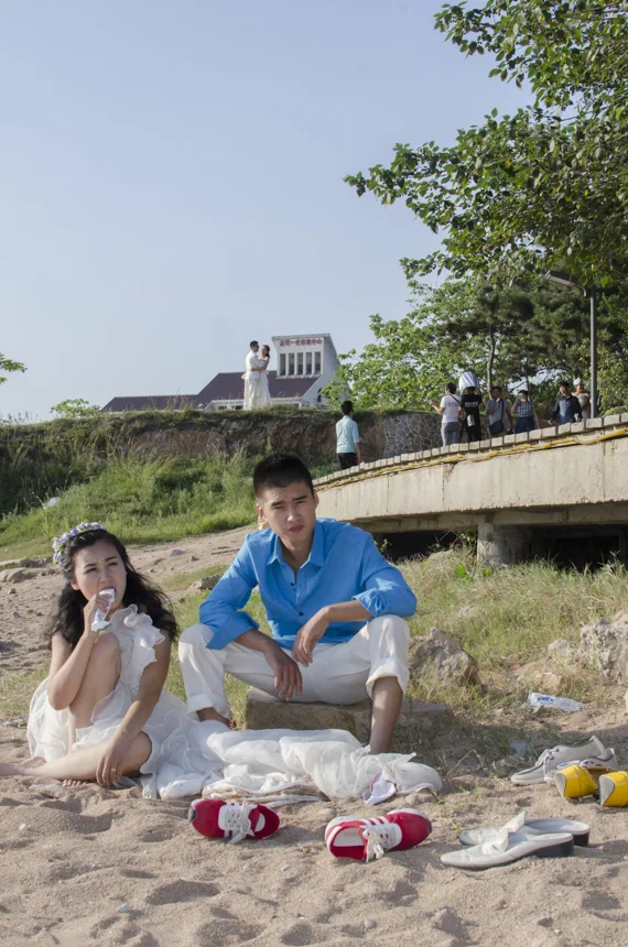 A couple sits boredly on the beach, waiting to be called by their photographer. 