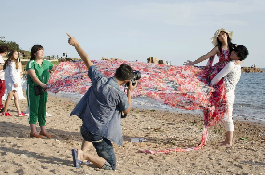 A man holds his fianceé up at the direction of their photographer. 