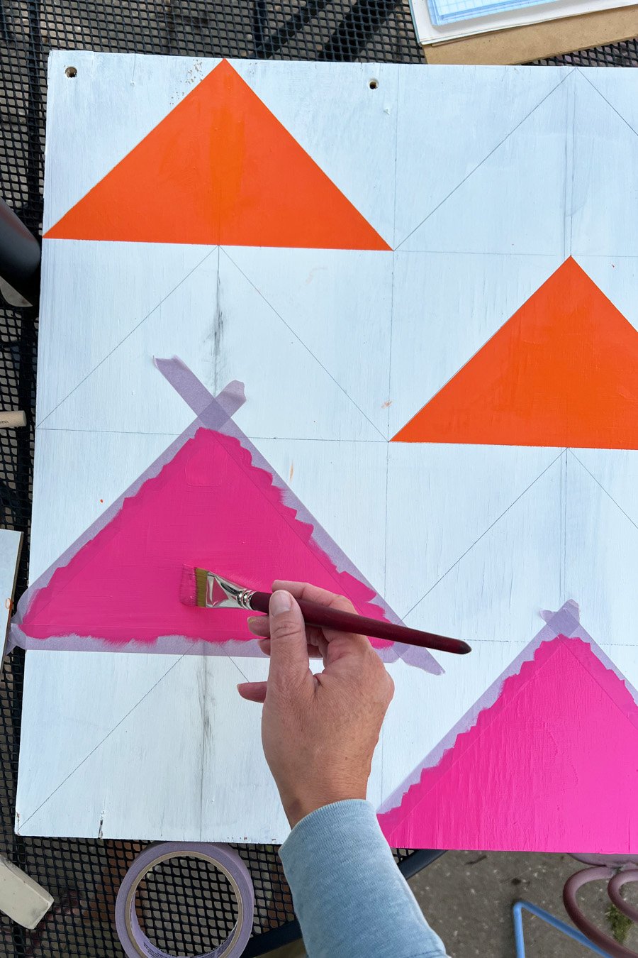 Painting pink and orange triangles on a wooden panel inspired by flying geese barn quilt designs