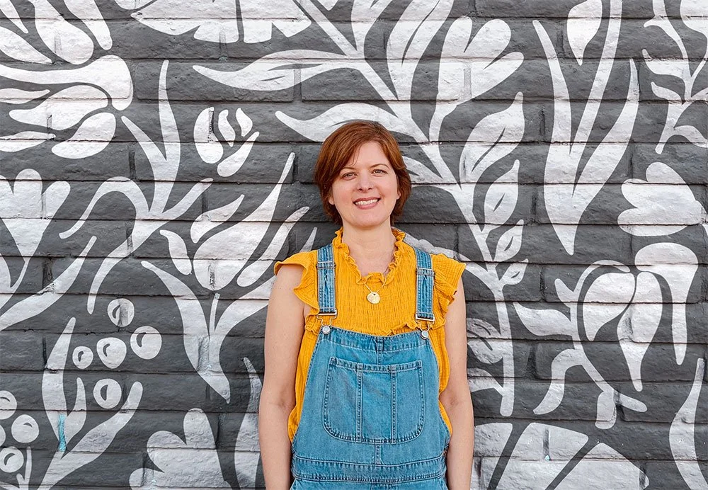 Artist Kim Koehler stands in front of a beautifully painted wall