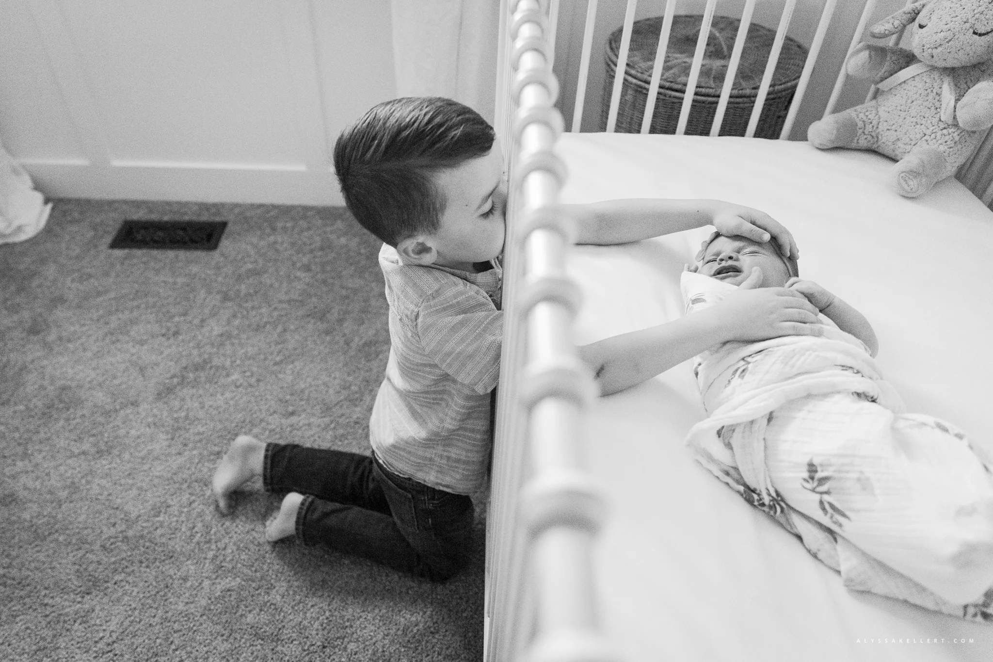 big brother reaching into crib to touch his baby newborn sister during photo session in mission bc