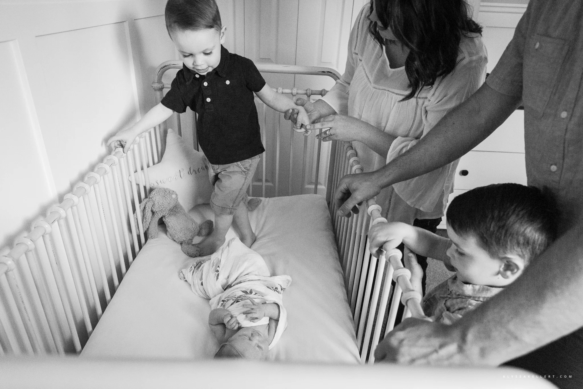 family reaching in to crib to see baby newborn girl during documentary session