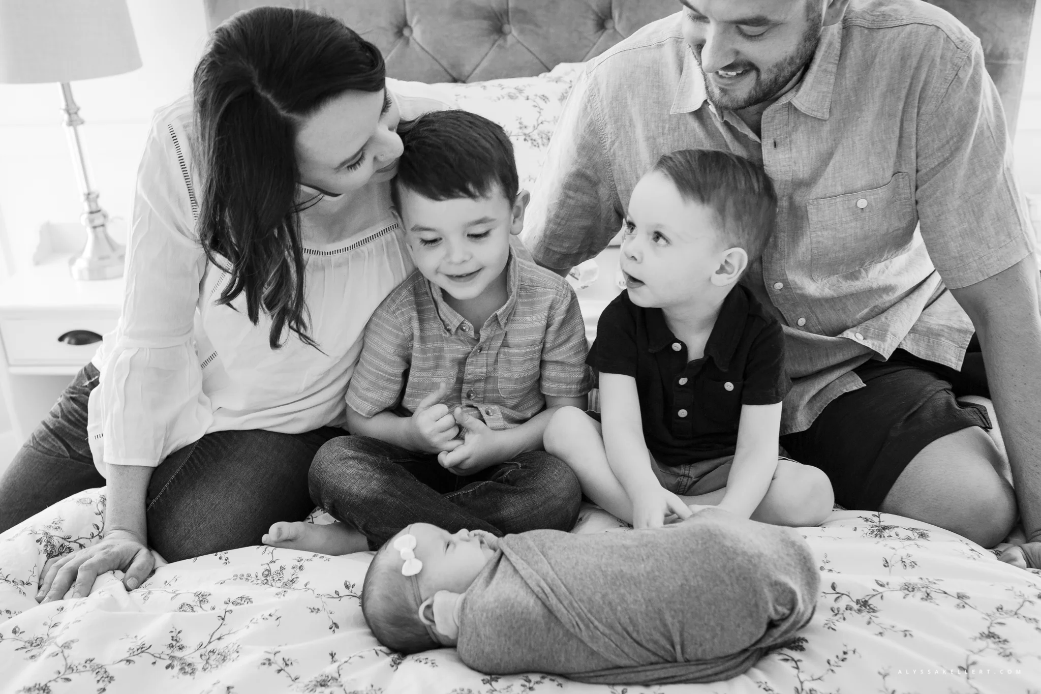 family on bed with newborn baby sister