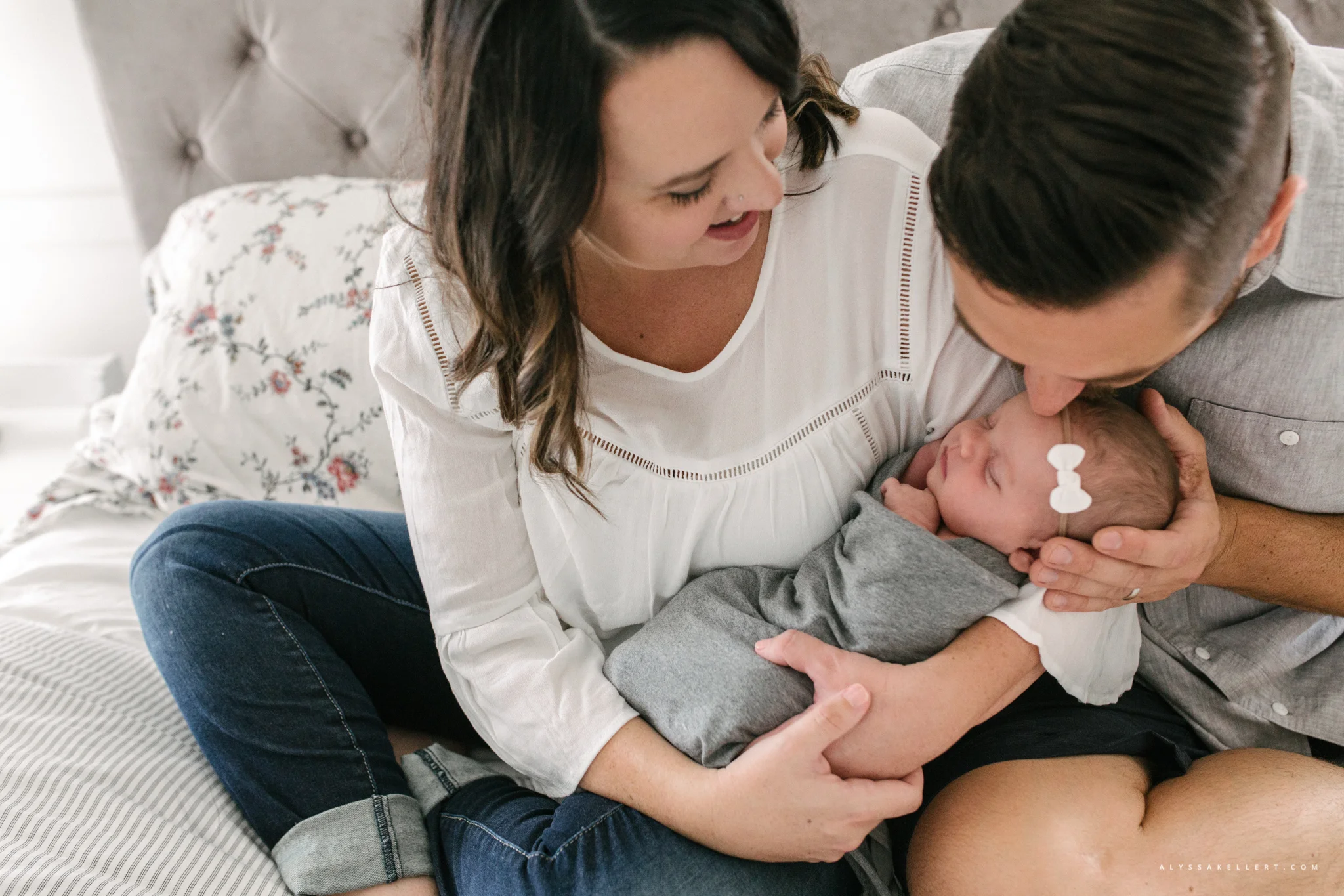 dad kissing baby girl while mom holds her in master bedroom lifestyle photography session