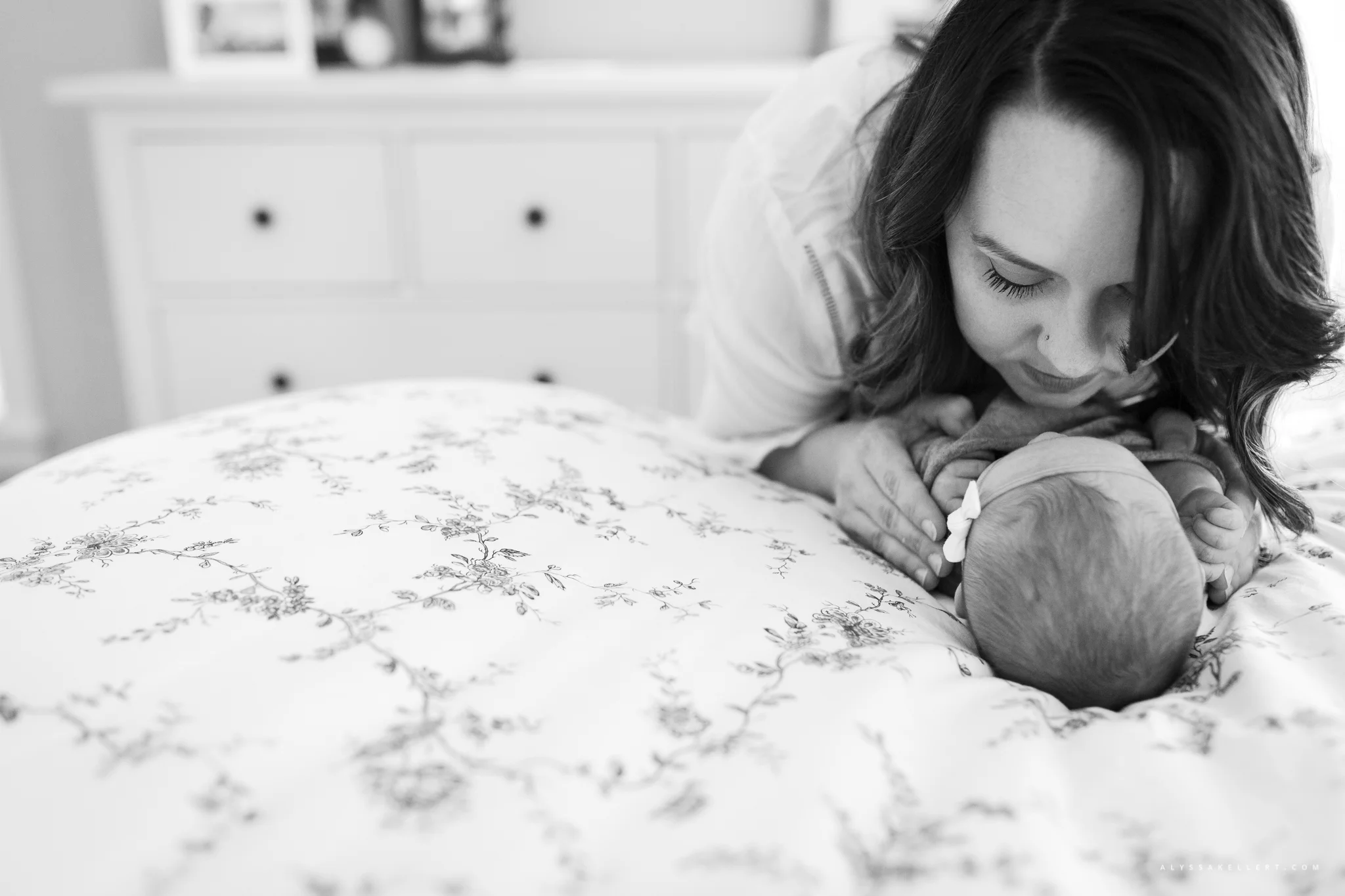 mom looking at her baby girl lying on the master bed during lifestyle photography session