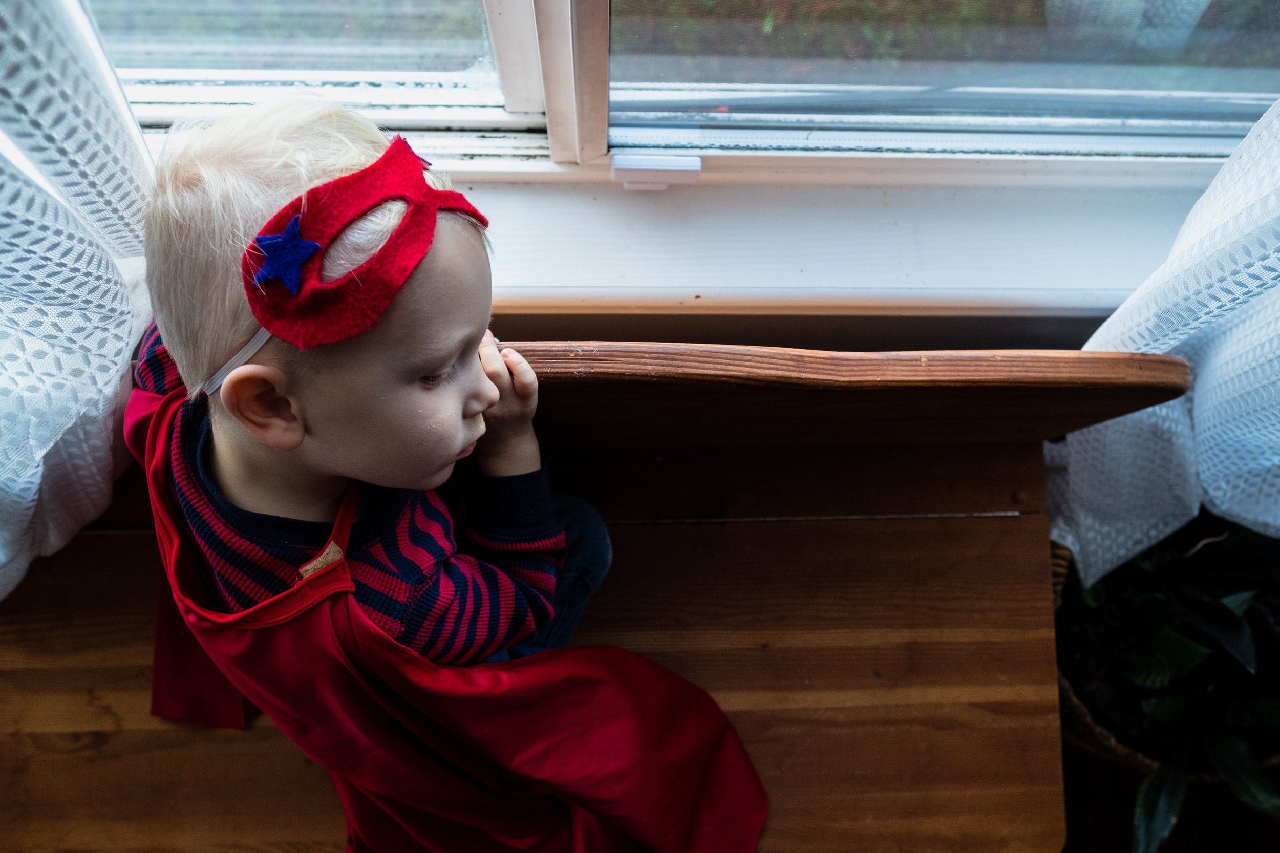 little boy in superhero costume gazing out of window in vancouver canada