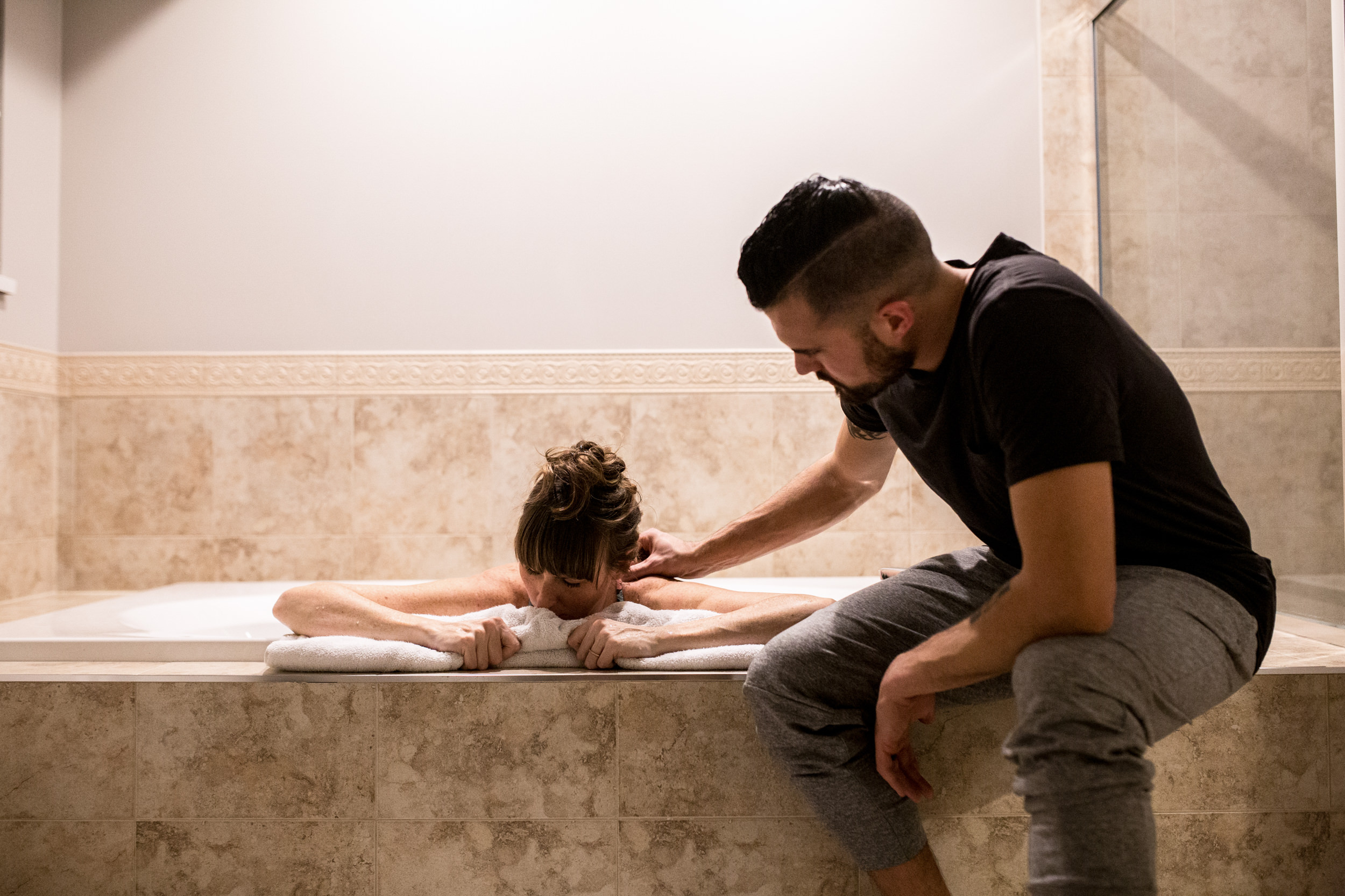 dad supporting mom in the bath tub with his hand on shoulder