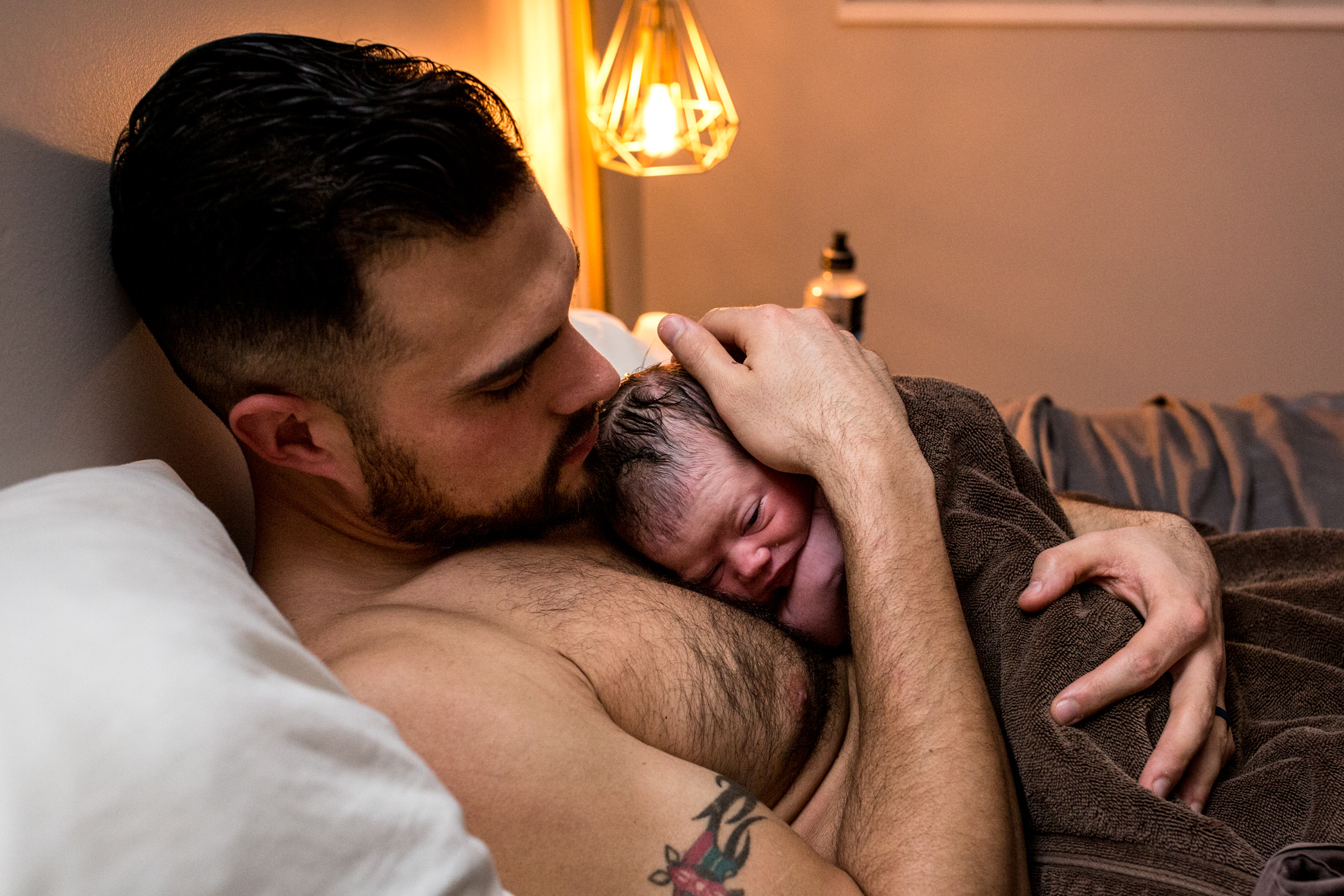 dad with baby on chest with lamp in background