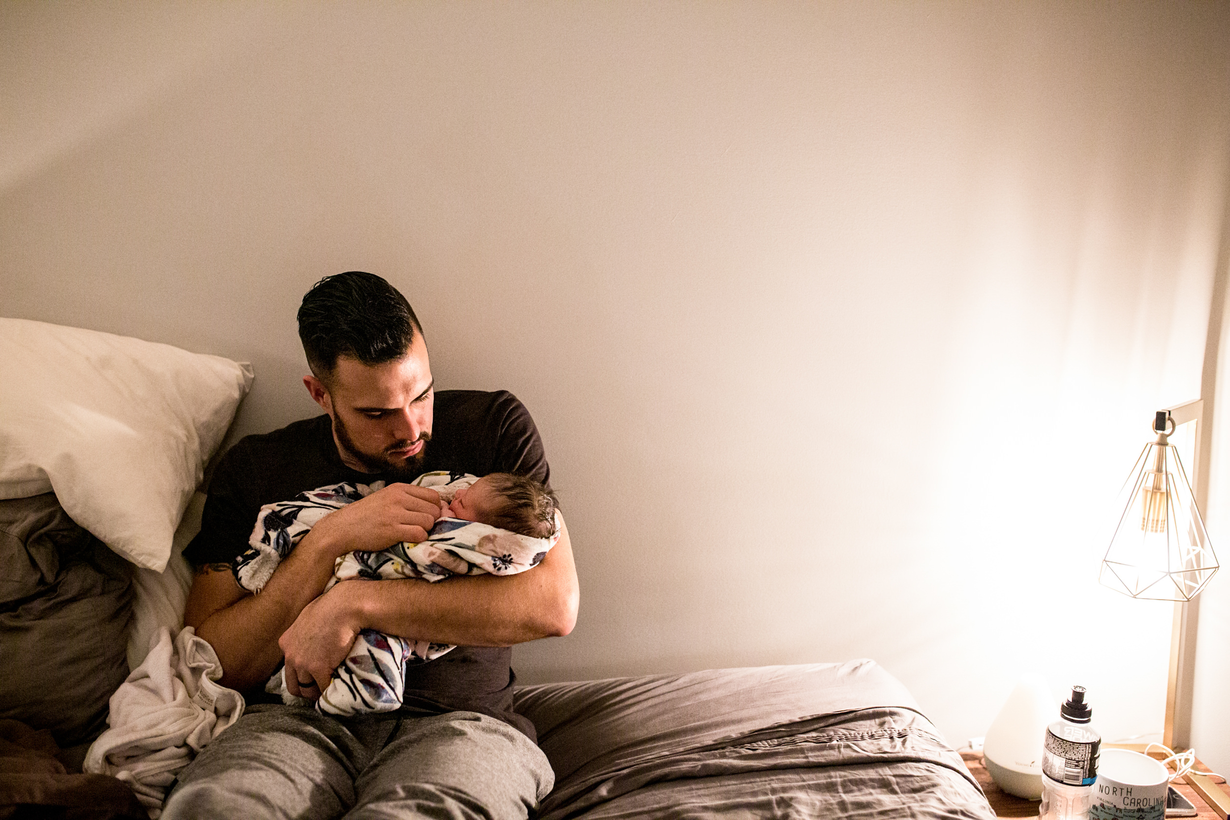 father holding his new baby on bed after home birth