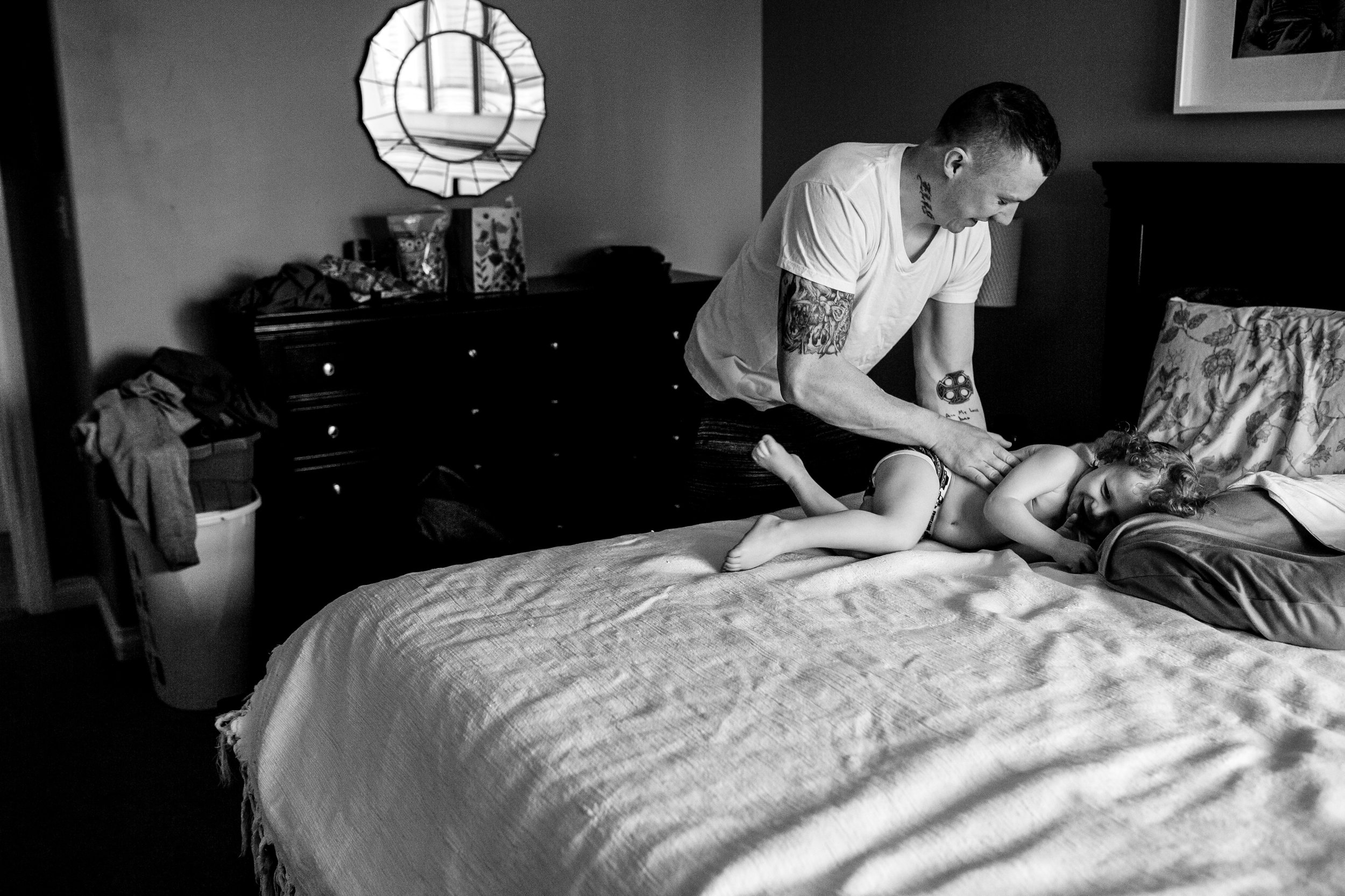 dad tickling toddler on the master bed