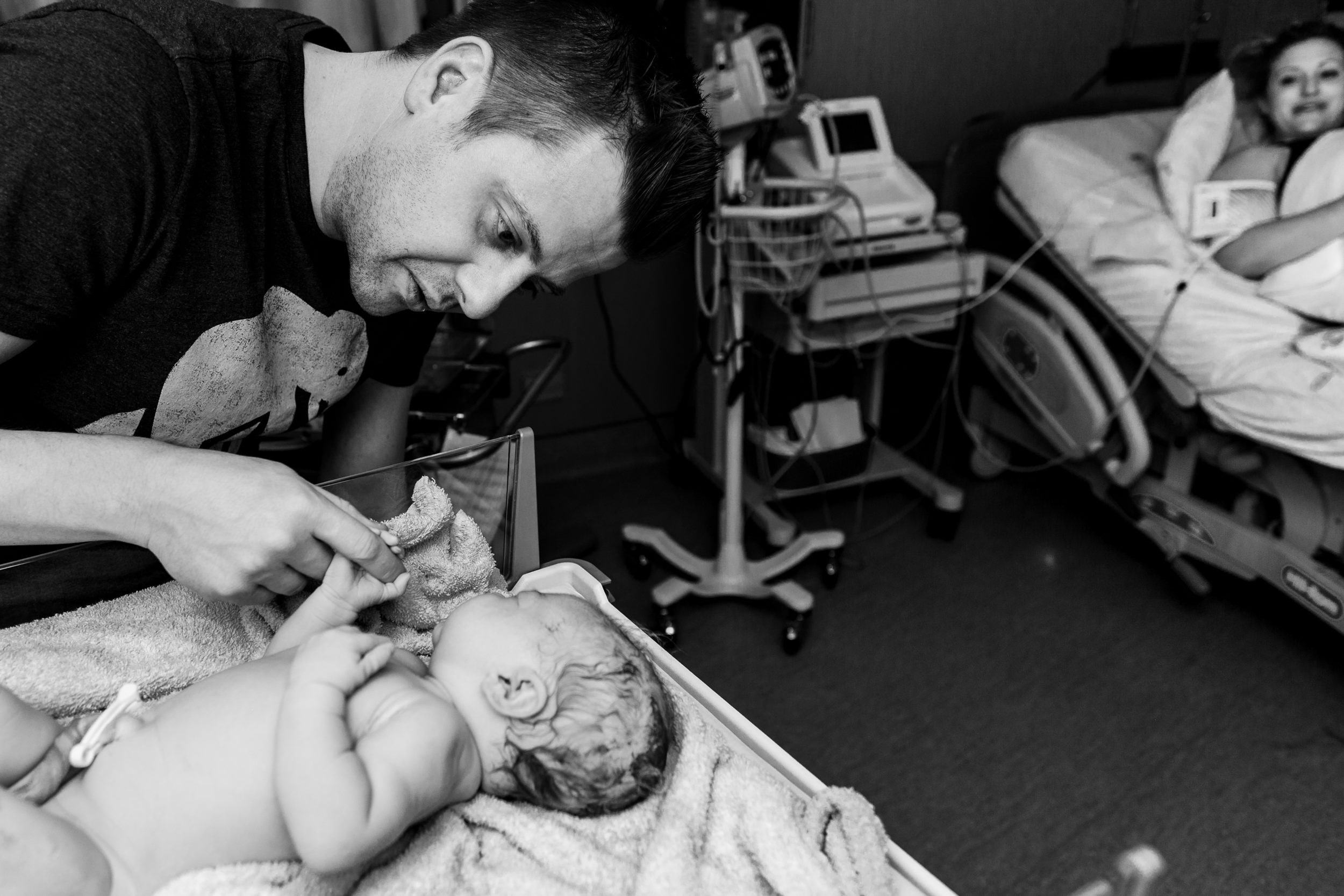 dad looking at newborn baby during exam with mom in the background