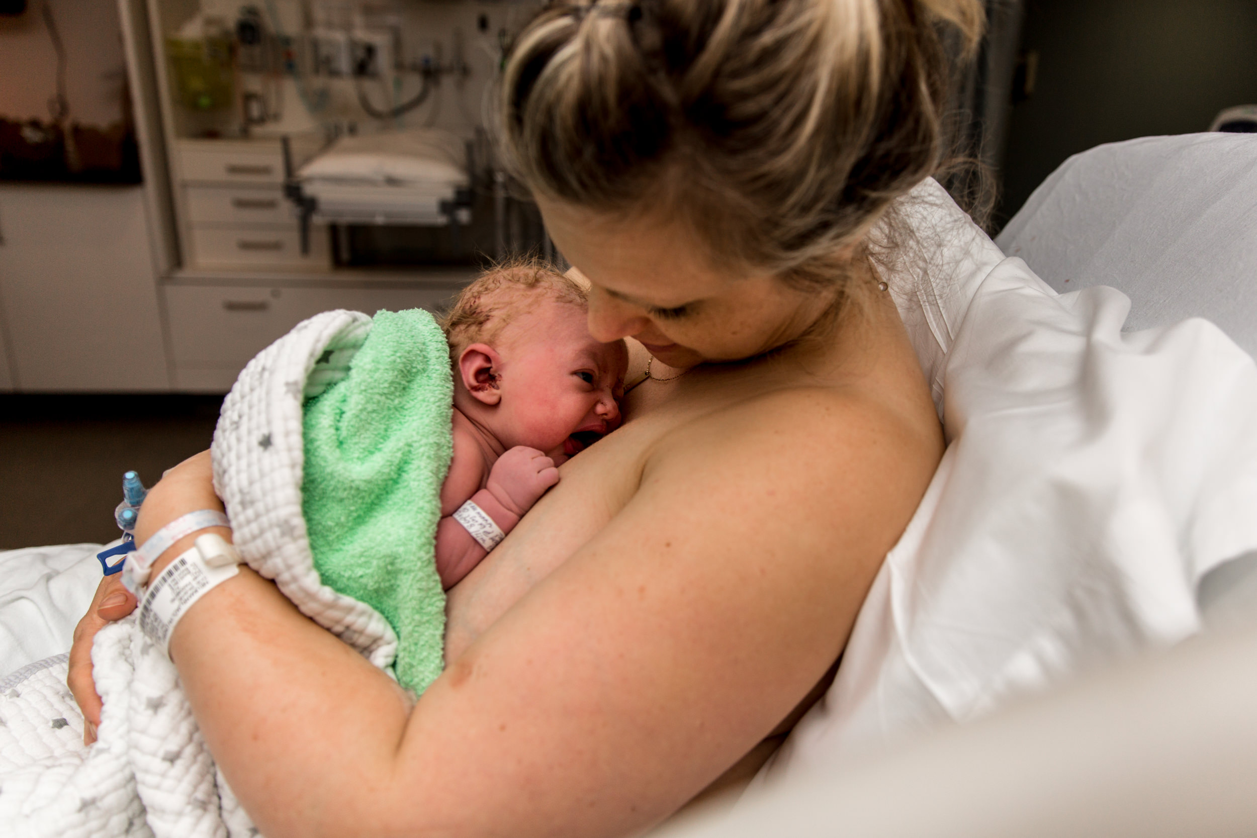 mom hugging newborn baby on hospital bed with green towel