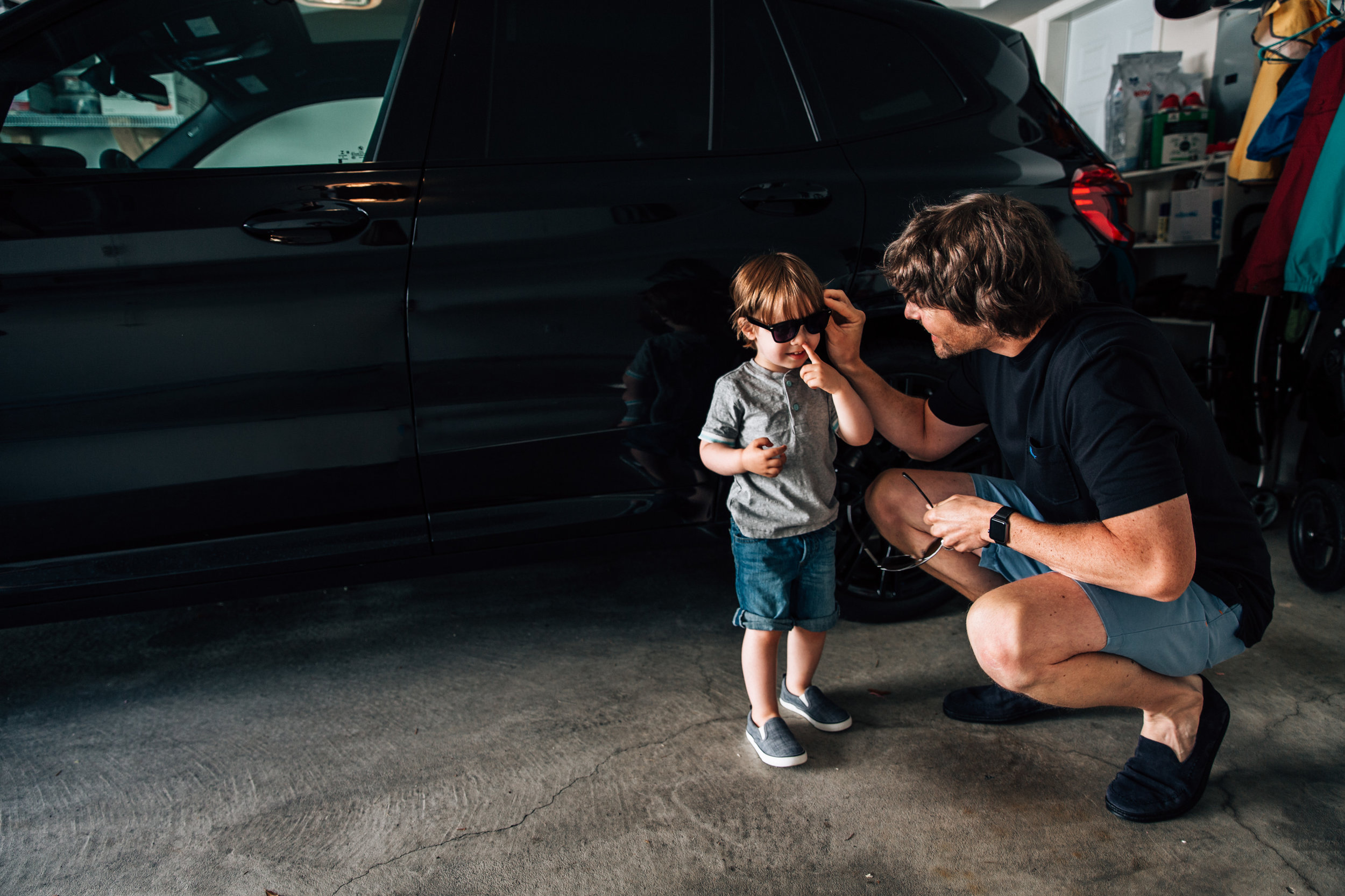 dad squatting down and putting glasses on young child in the garage