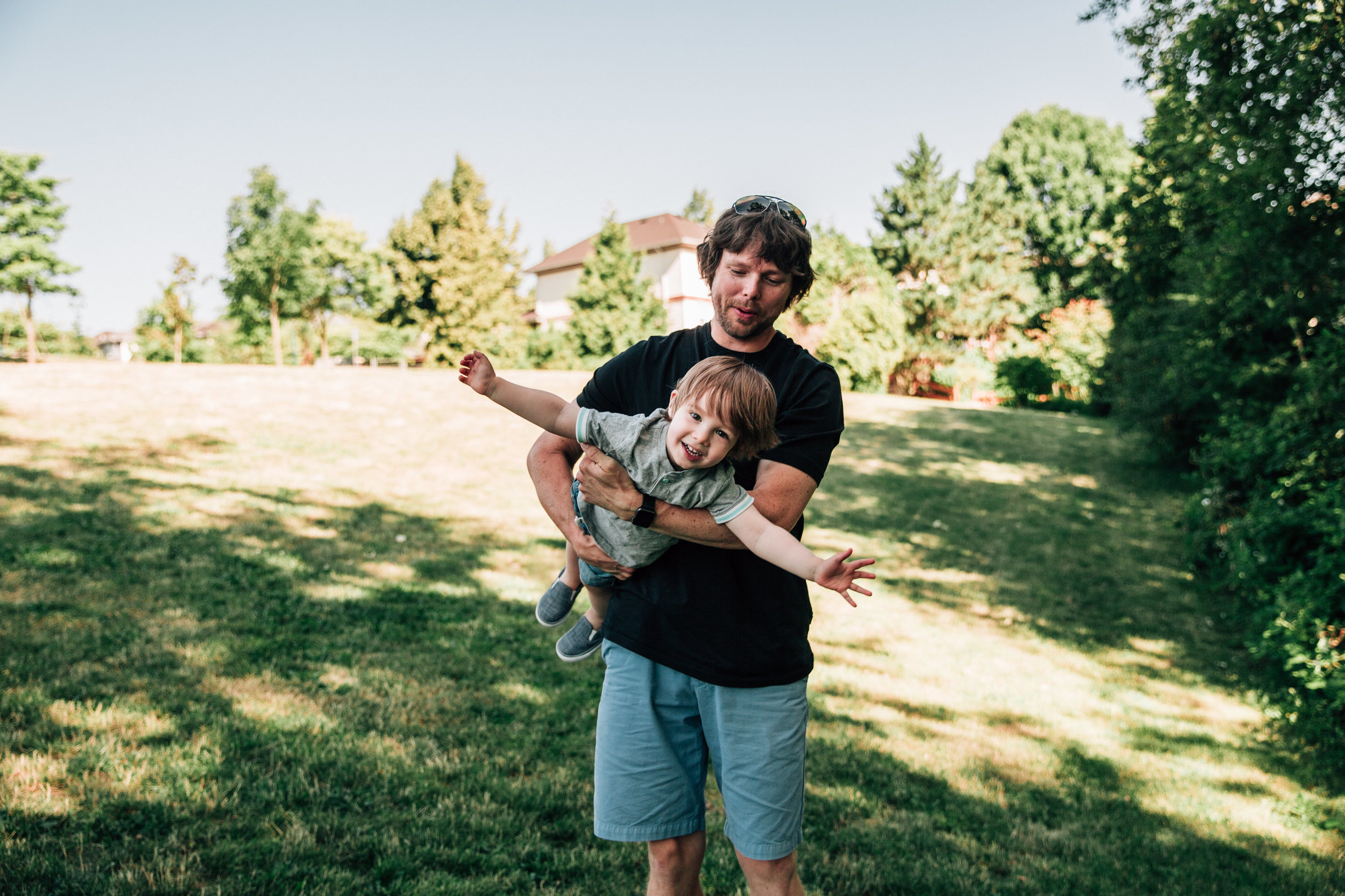 dad flying toddler on grass in his arms
