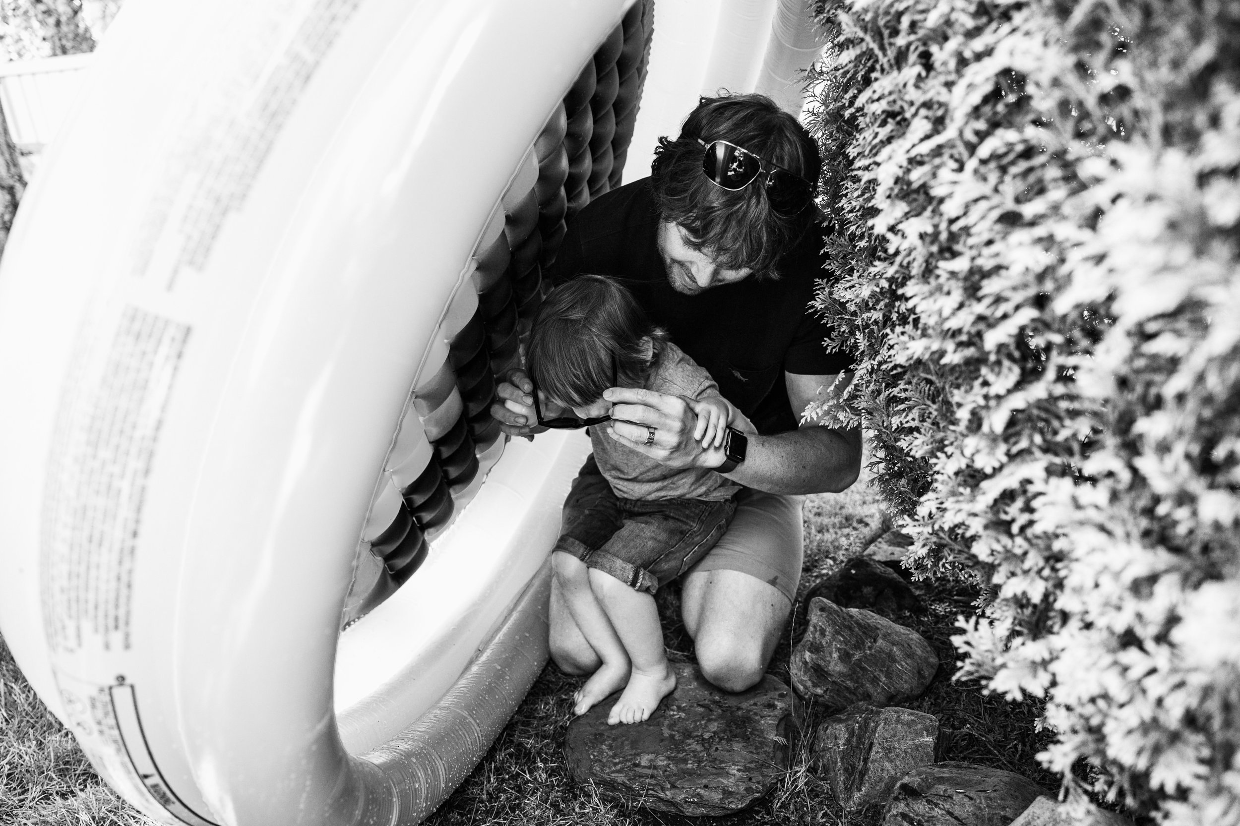 dad putting glasses on toddler under a standing inflatable pool