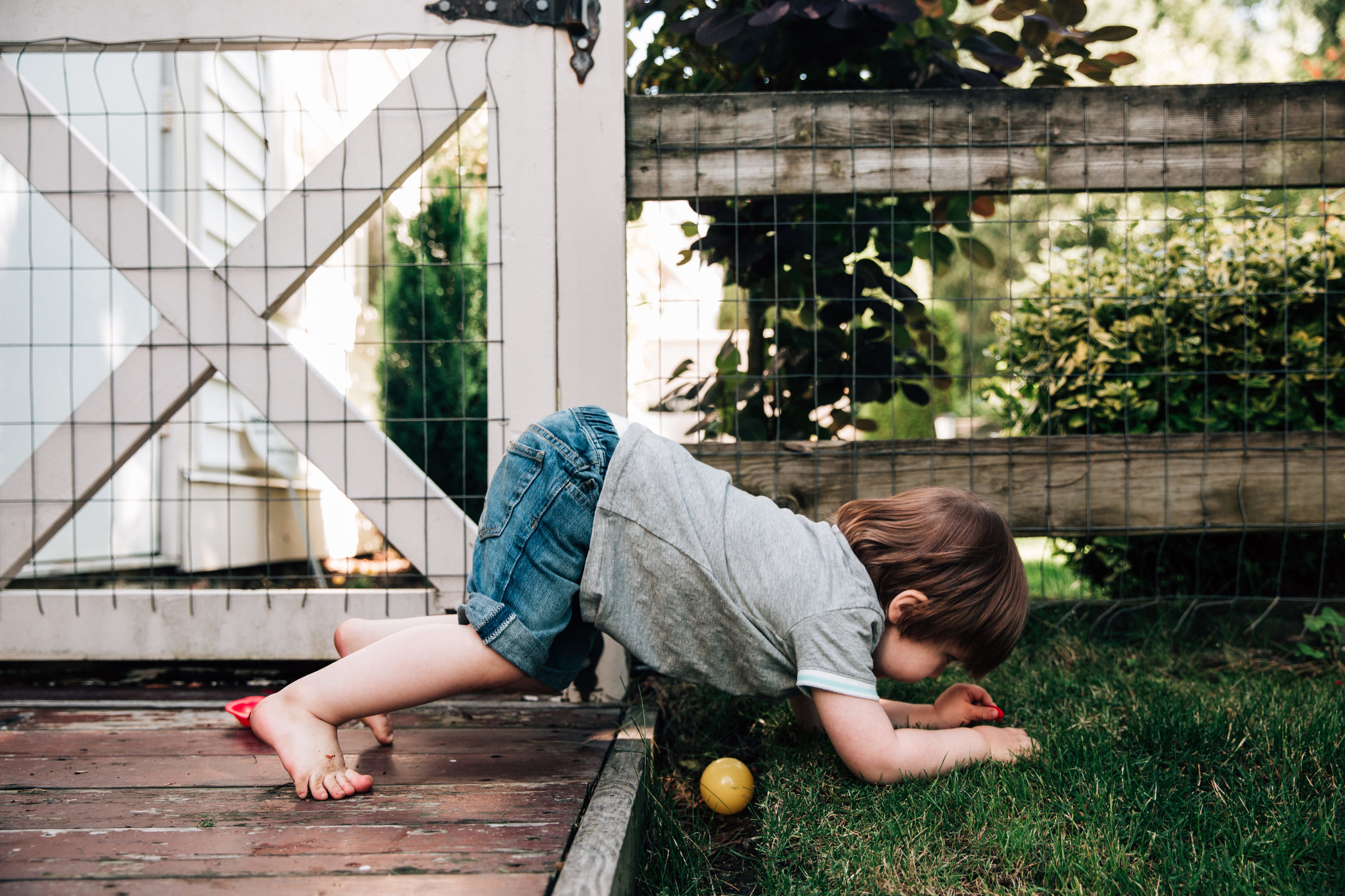 toddler on all fours climbing over a small ditch with a ball in it