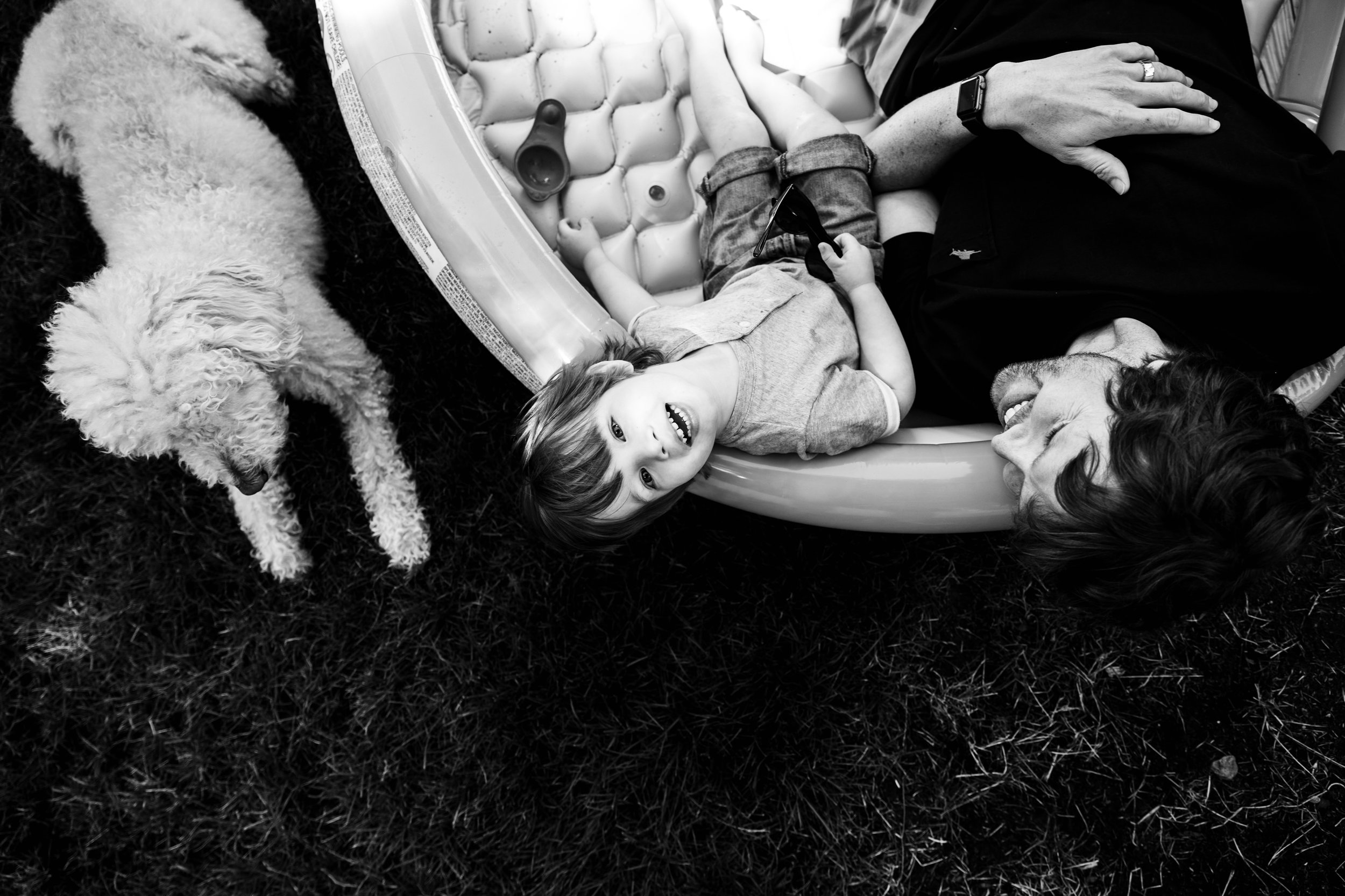 dad, son and dog leaning backwards out of an inflatable pool