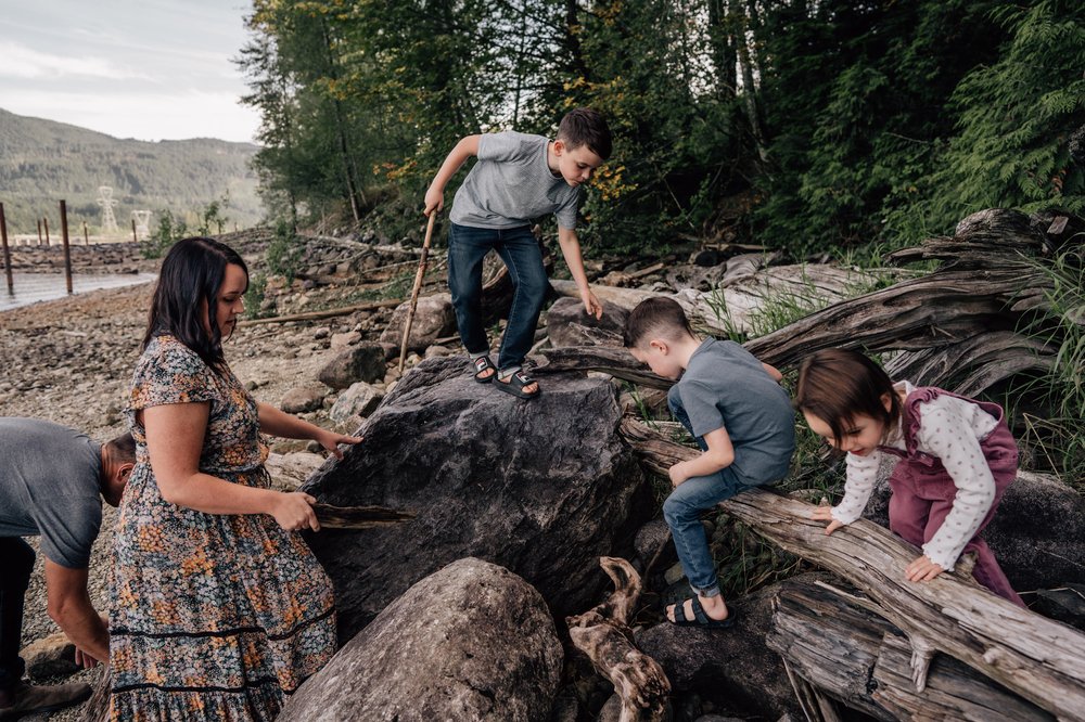 kids climbing on rocks and logs on a rocky beach with mom in a floral dress keeping watch in calgary