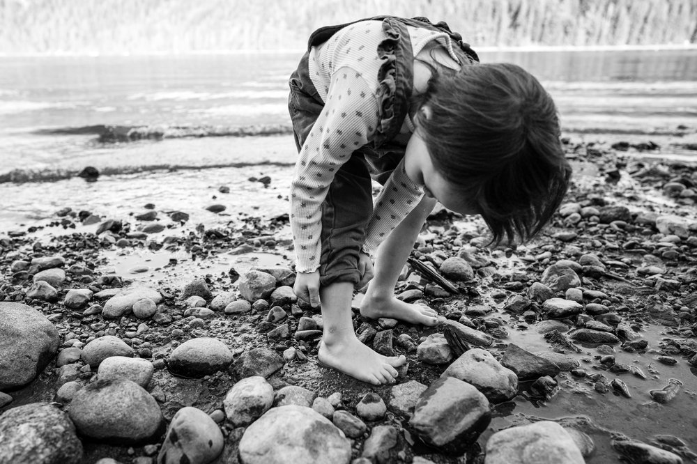 black and white image with young girl rolling up her pant legs to go in the water on a rocky beach