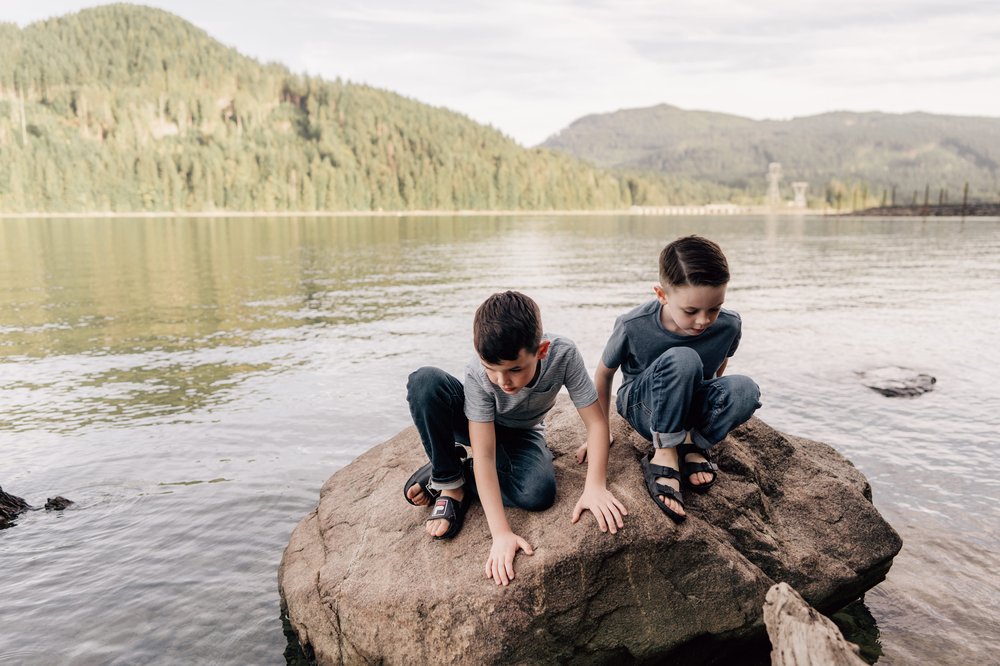 two young boys climbing on a big rock in the water at a lake in the mountains alberta