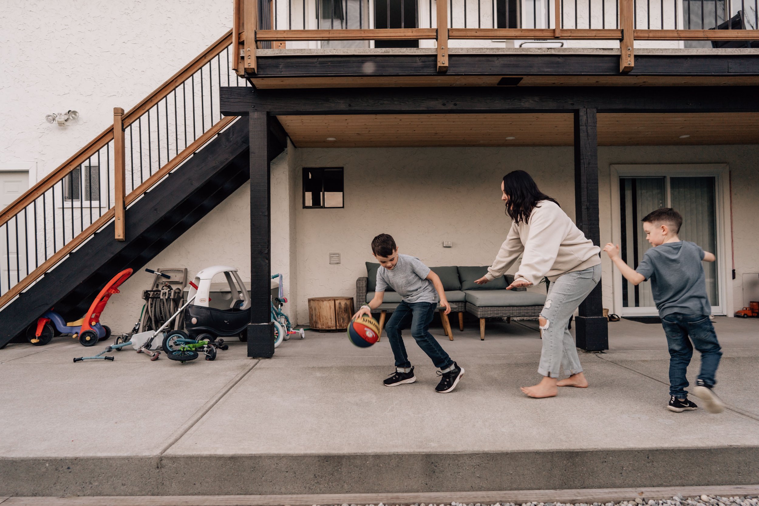 mom playing basketball with two sons in their back yard