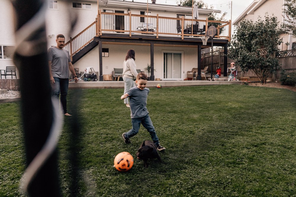 boy playing soccer with mom in back yard through the net