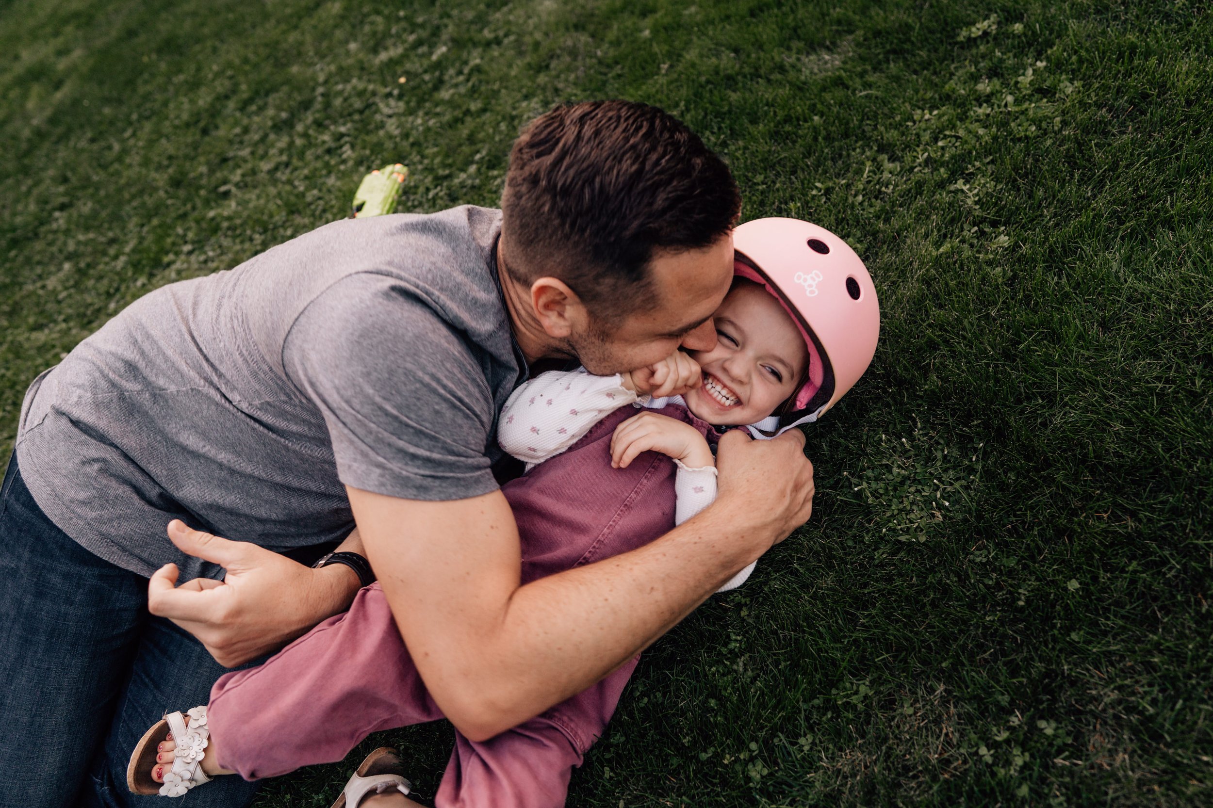 dad kissing young daughter while she laughs in the grass
