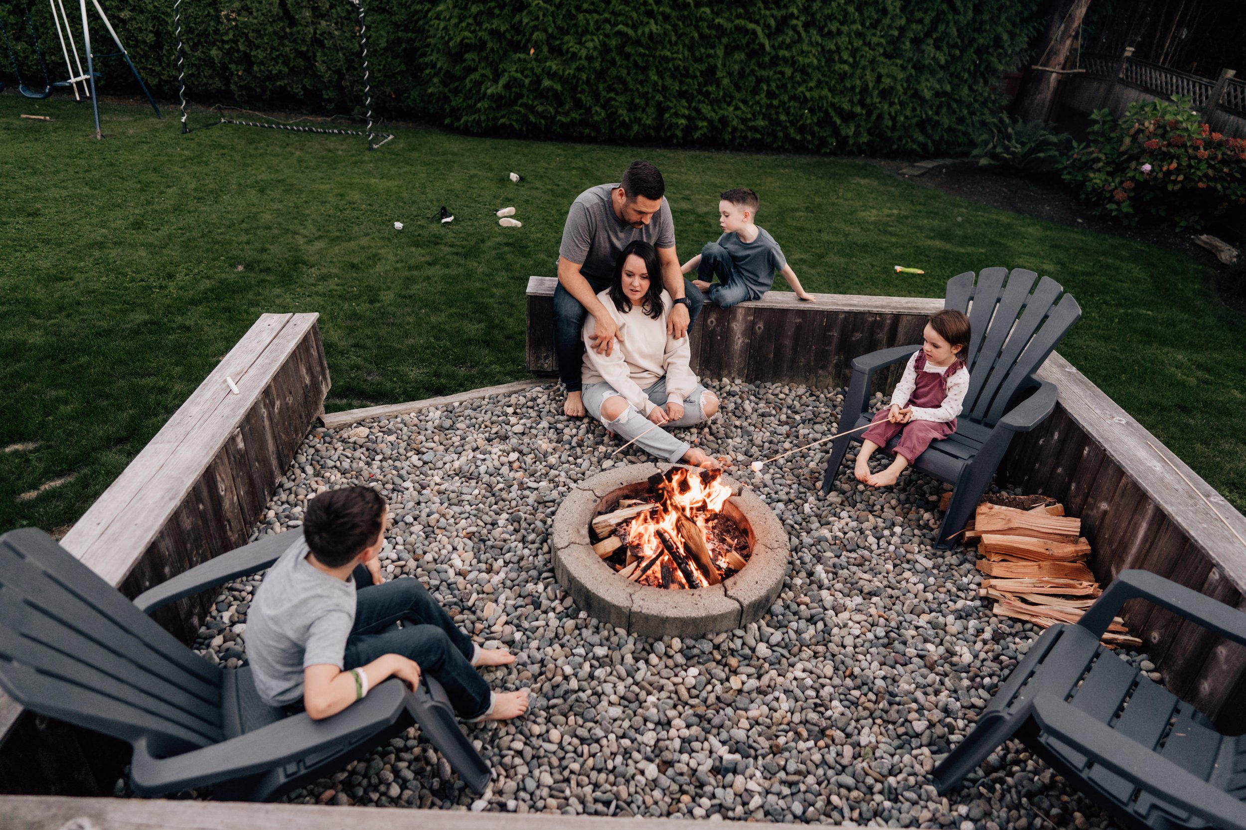 family of five sitting around back yard camp fire roasting marshmallows near rocky mountains 