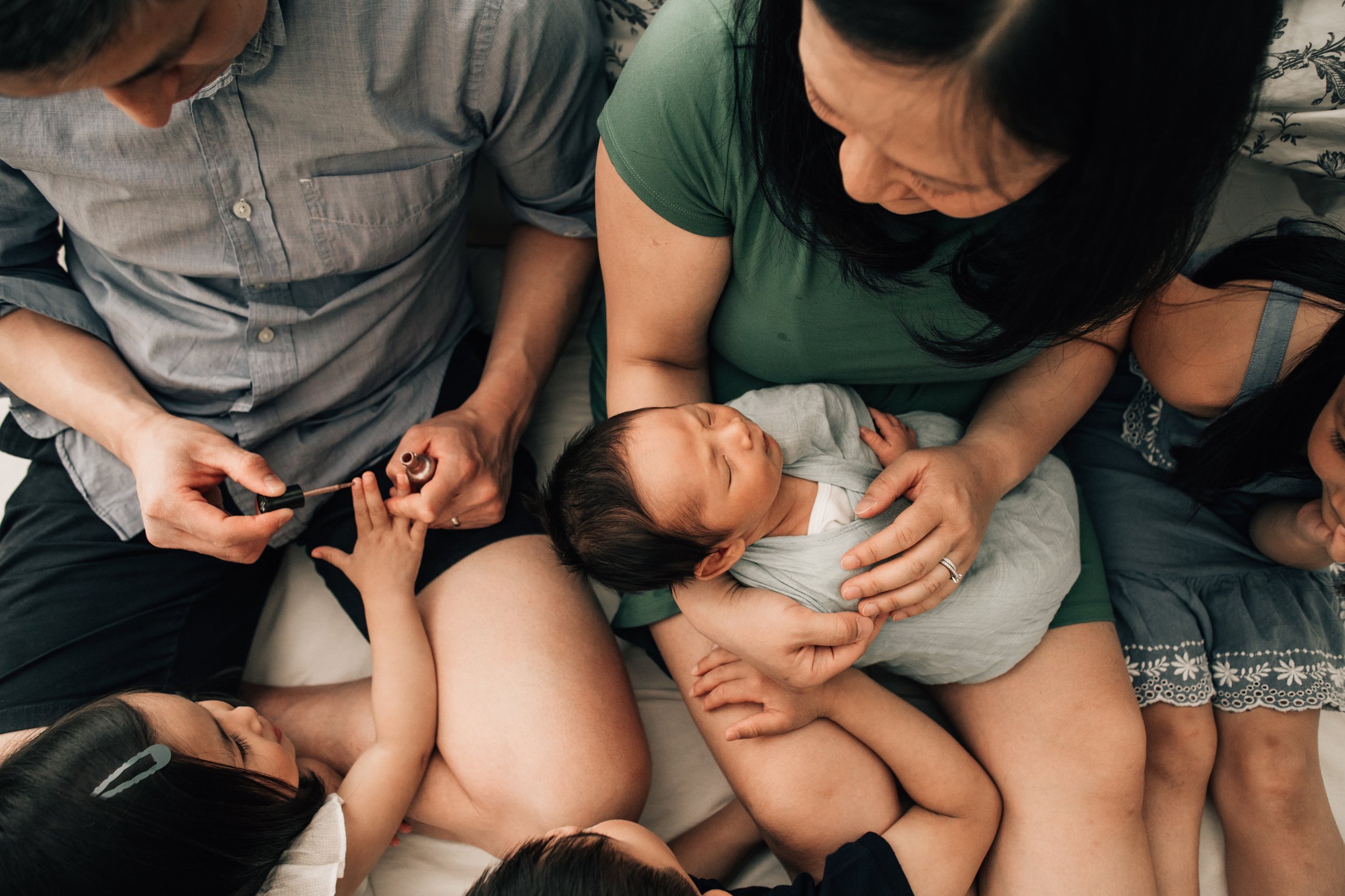 family together with newborn with dad painting toddler's nails in Airdrie