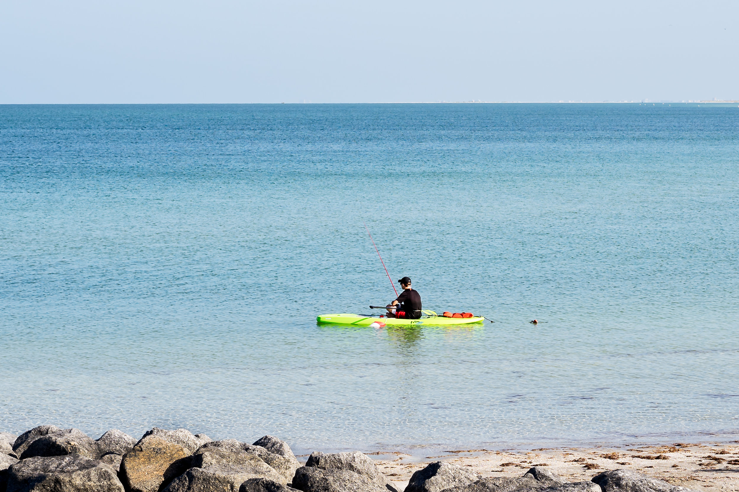 A young man fishing off his kayak and taking advantage of the great spring weather. The rock outcroppings are a great place to catch fish in this area. Fort Desoto offers kayak and canoe rentals by the hour or for the entire day. 