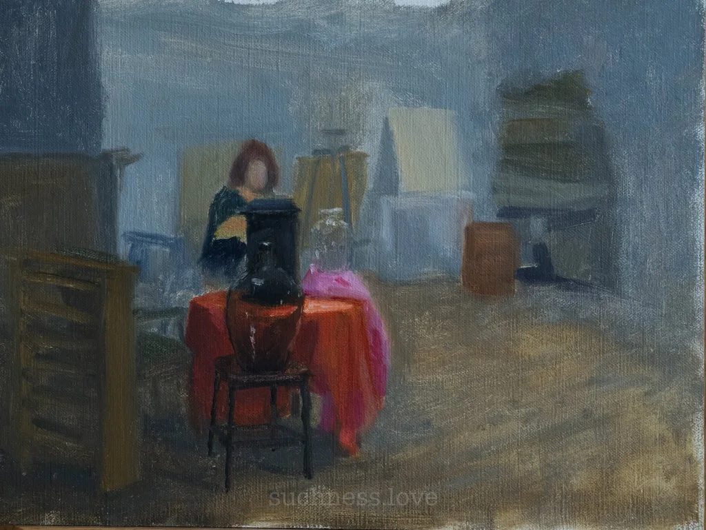 A woman with red hair sitting at a round table with a red tablecloth in a room with various art supplies and furniture.