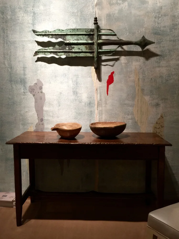 This vignette by Robert Young Antiques incorporates a graphic early banner form weathervane and two antique carved bowls placed atop an unusual banded single plank tavern table.