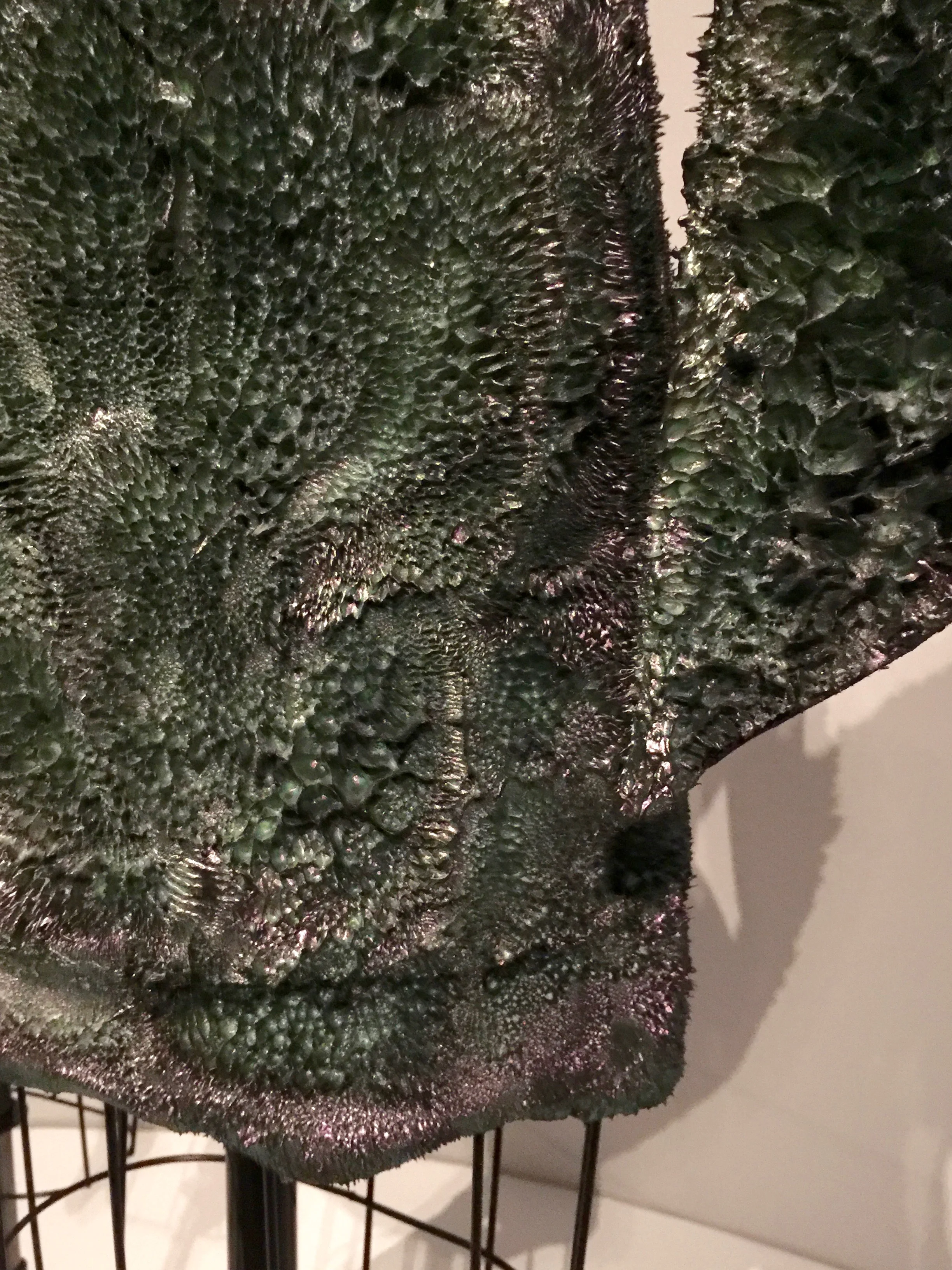 "(This) dress has a base made from cotton fabric. Then there is a rubber component- a soft rubber- in which we place metal powder. When you mix everything together, the rubber has a few minutes when it is still wet and soft. We pour the rubber onto the cotton fabric. then we place magnets above and below, and you see the metal powder grow piece by piece- in a matter of seconds before it sets. The coloration is exquisite because while the rubber is still wet and soft we add a very thin enamel powder that has iridescent qualities." - Iris van Herpen