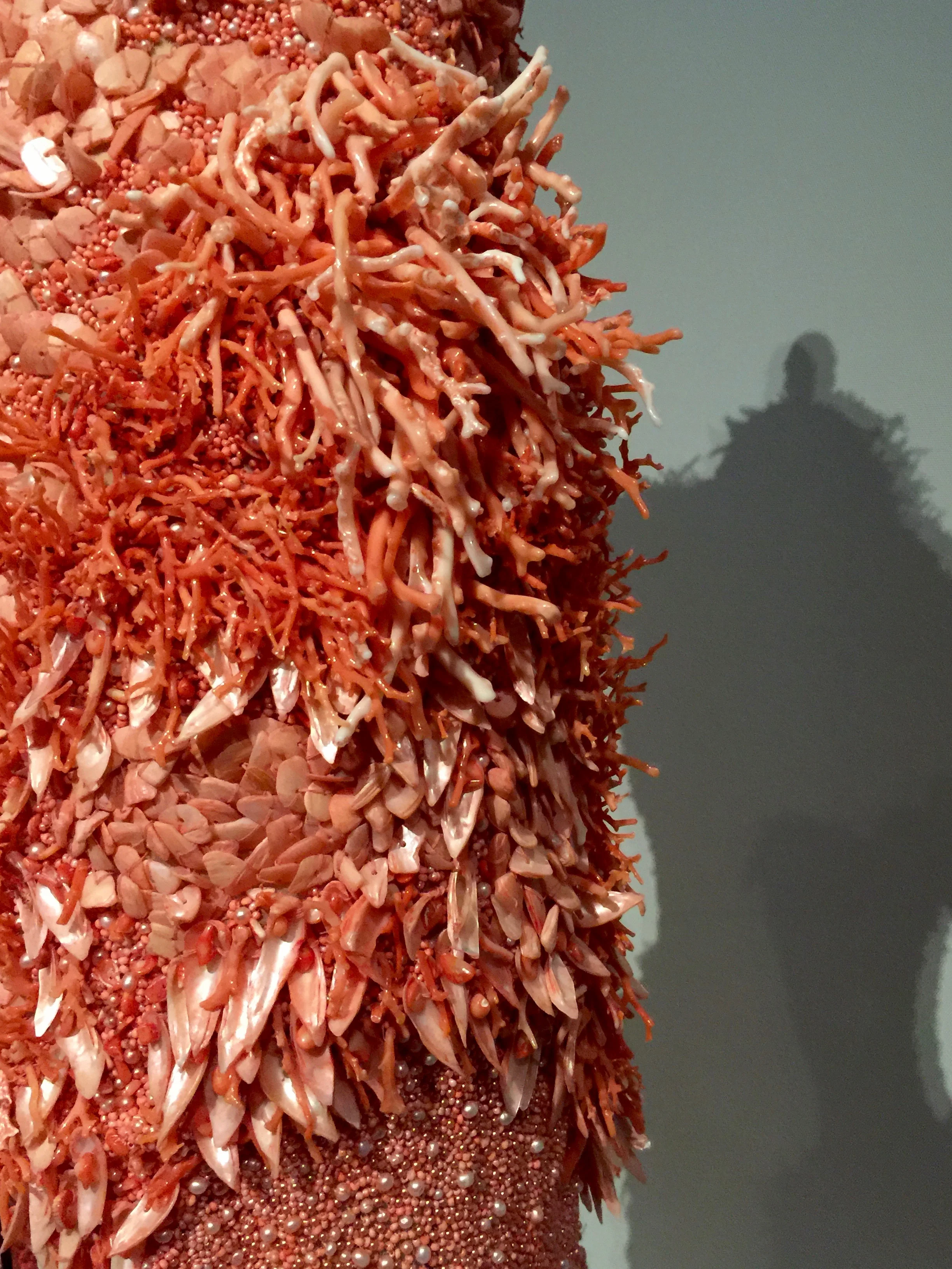 Details of the Alexander McQueen nude silk organdy and net dress which has been hand-embroidered with red-orange glass beads, freshwater pearls, pieces of coral, and dyed shells.