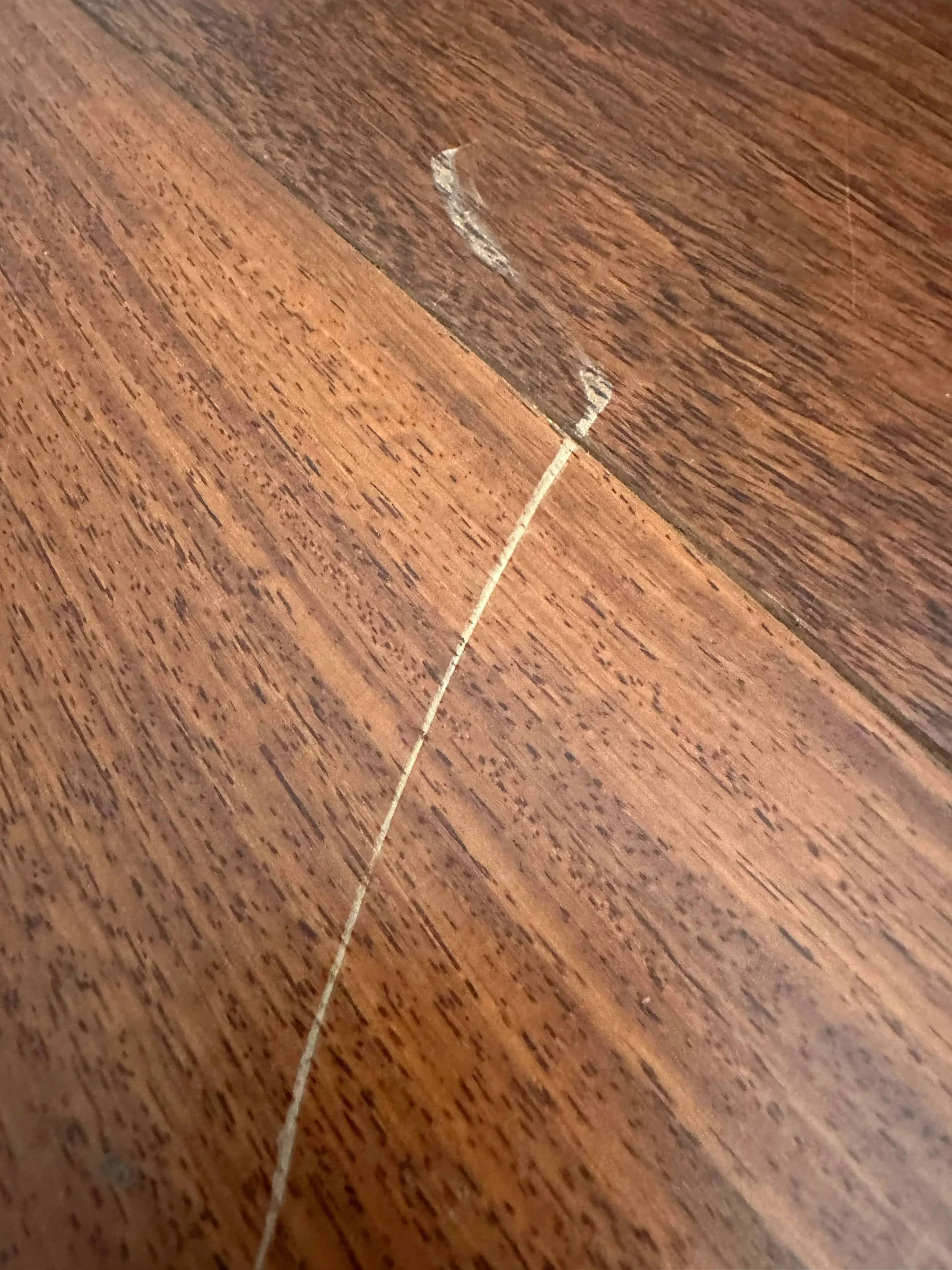 Close view of scratches and wear on a hardwood floor before restoration