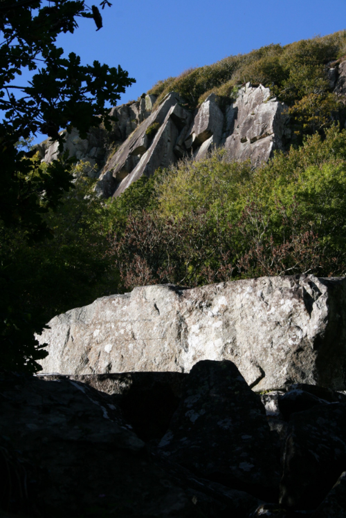 Looking up to the distant crag of slanting slabs with overhangs.