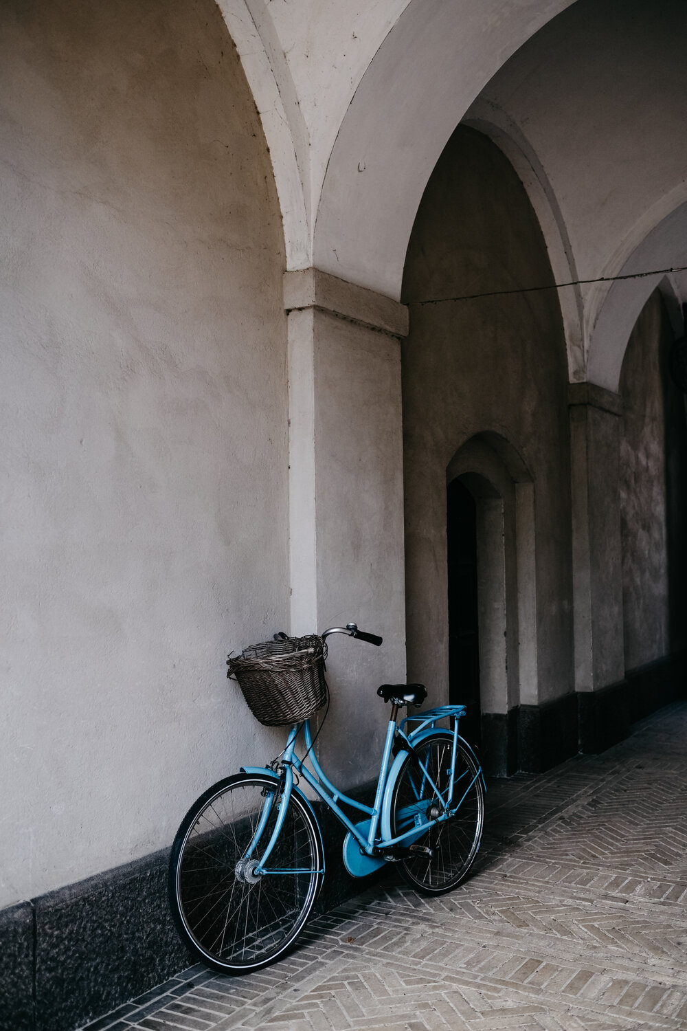 A blue bike parked under arches on a herringbone brick walkway