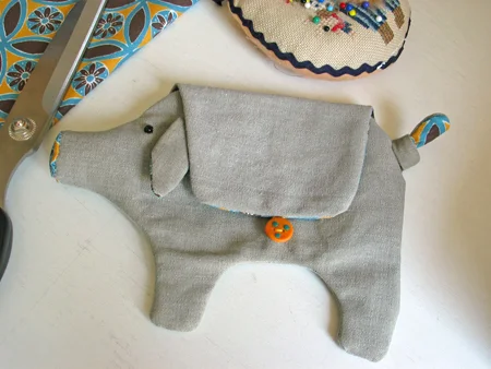 Step 5. Turn everything right side out and attach the ears. Sew on beads for the eyes and make a knot in the tail. Make a little loop for the button with embroidery floss. Sew the button in place. You might want to put some stuffing in his nose.
