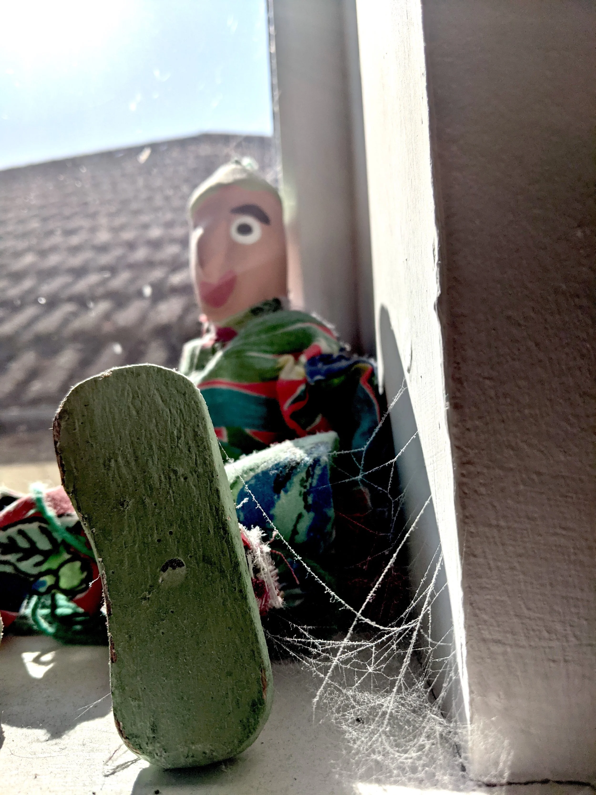 wooden toy sat by the window, a spider web connects its foot to the wall