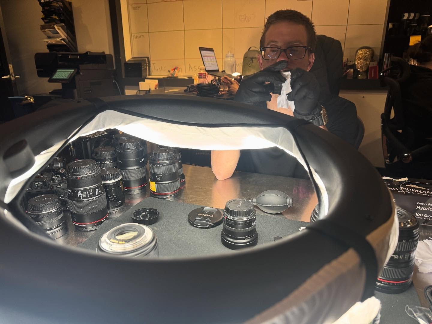 Behind the scenes, Gabe keeps our camera lenses sparkling clean! ✨ 💖 🧼 
.
.
.
.
Photo Caption: Gabe, a Prospect, wears gloves and works under a large LED light wiping down camera lenses. #WorkingIsWorking #SparkleOn #MediaProduction