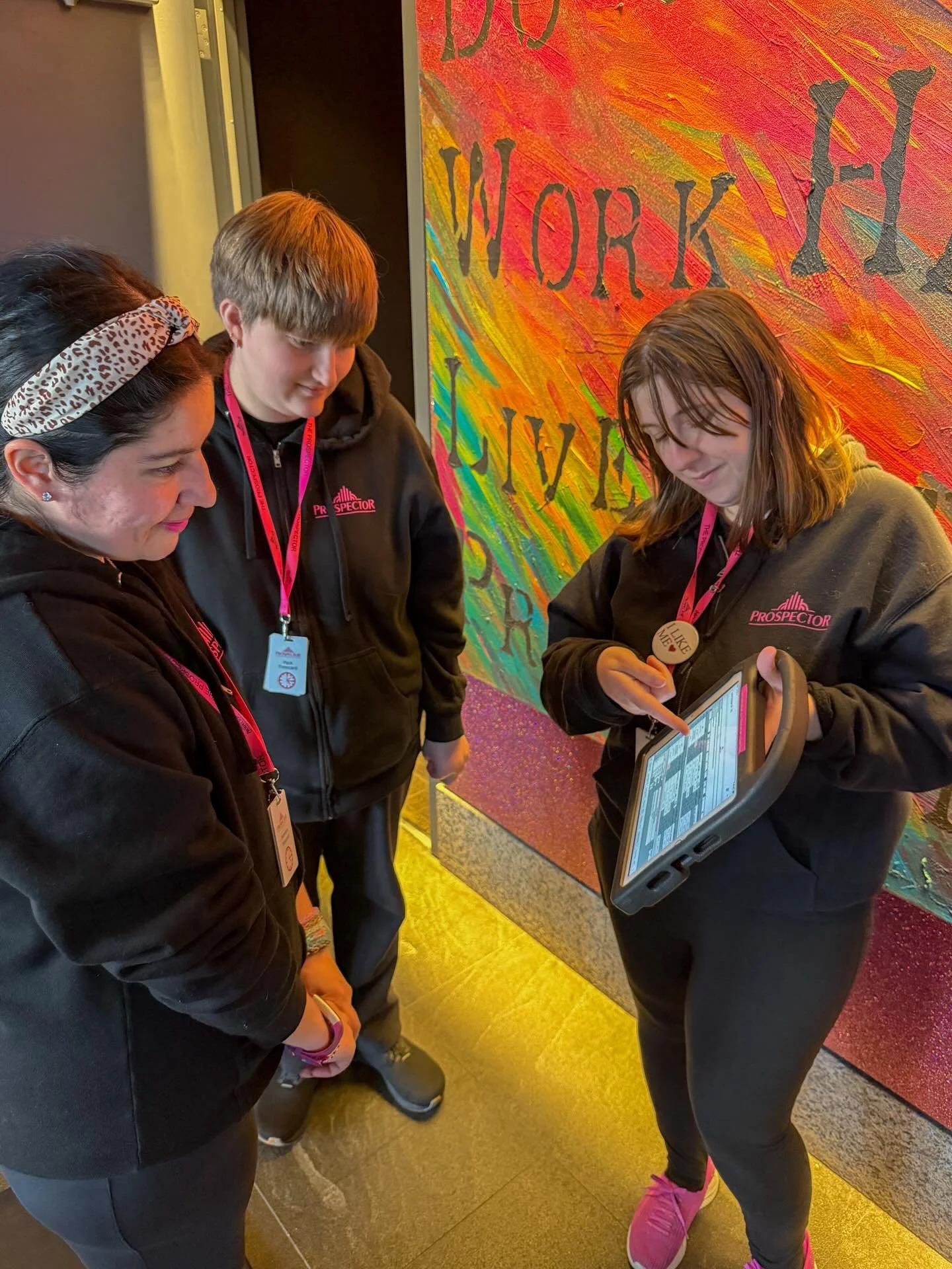 Amanda teaching and training two of our newest ushers, Chrissy and Maya. ✨
.
.
.
.
.
Photo Caption: Three Prospects stand in the lobby of The Prospector, looking at a training tablet. Chrissy, with dark hair and pink lipstick, is on the left. While M