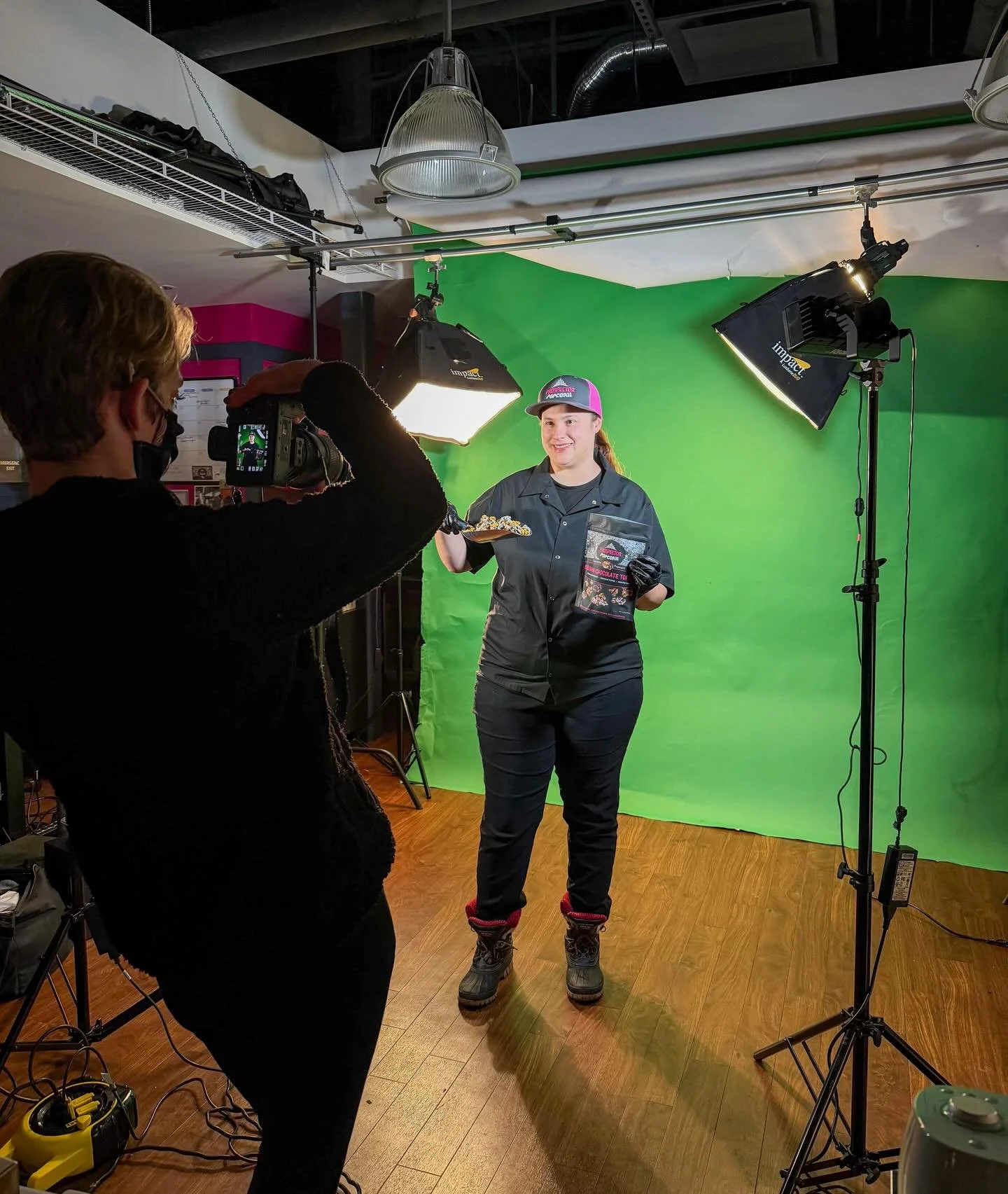 Behind the scenes, Ali takes photos of Jenny for our seasonal banners. ✨📸 
.
.
.
.
.
Photo Caption: Ali and Jenny are having a photoshoot in the training room at The Prospector. Jenny smiles while holding a bag of gourmet popcorn in her left hand. I