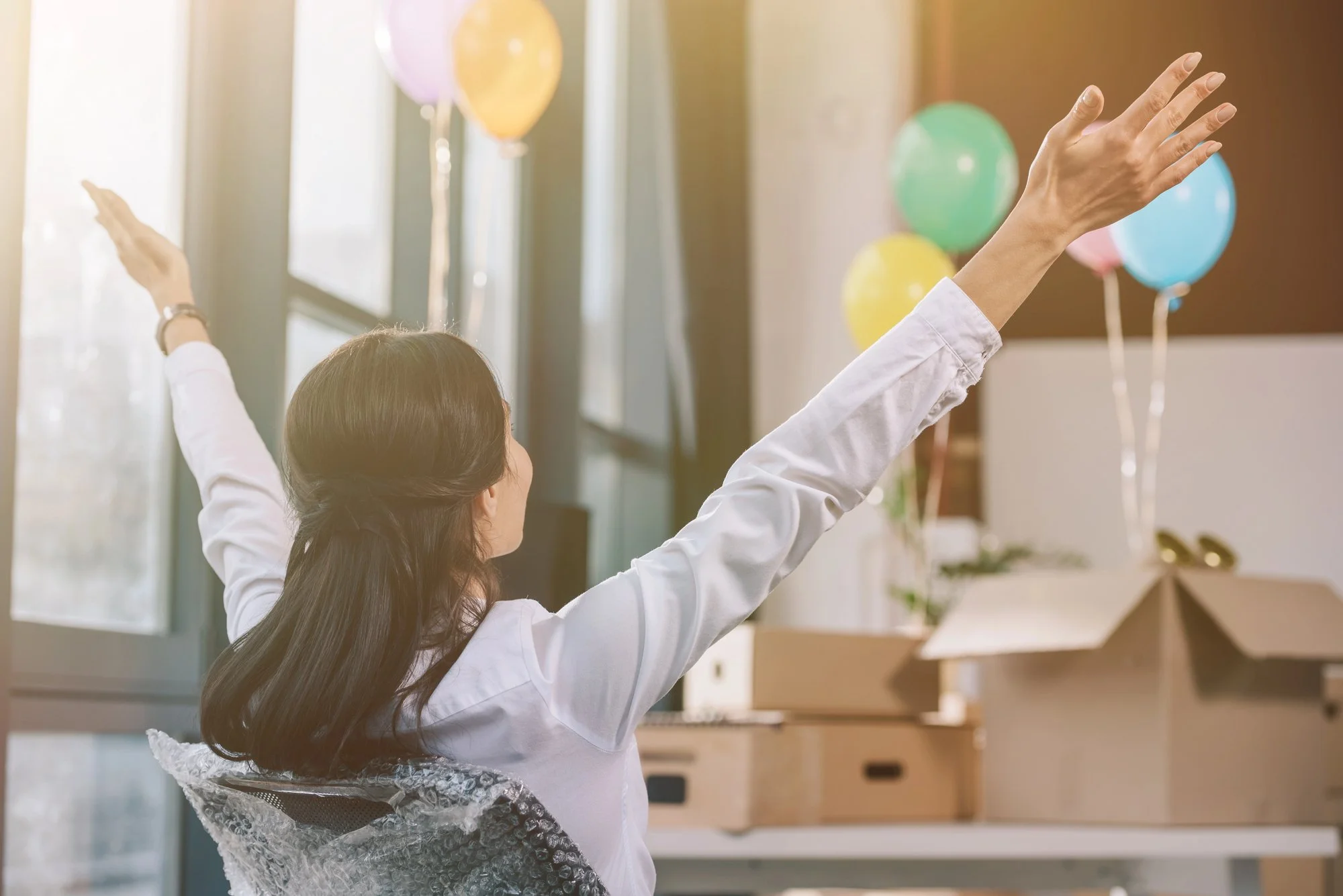 Woman celebrating a new office location with moving boxes and balloons, representing business growth, office relocation, client service expansion, and a welcoming new workspace in Farmington Hills.