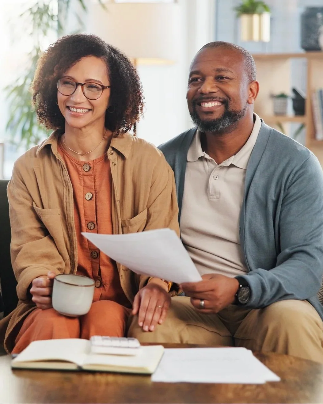 Two people meeting with a financial planner in a comfortable office setting, reviewing documents and discussing financial planning goals and long-term strategies.