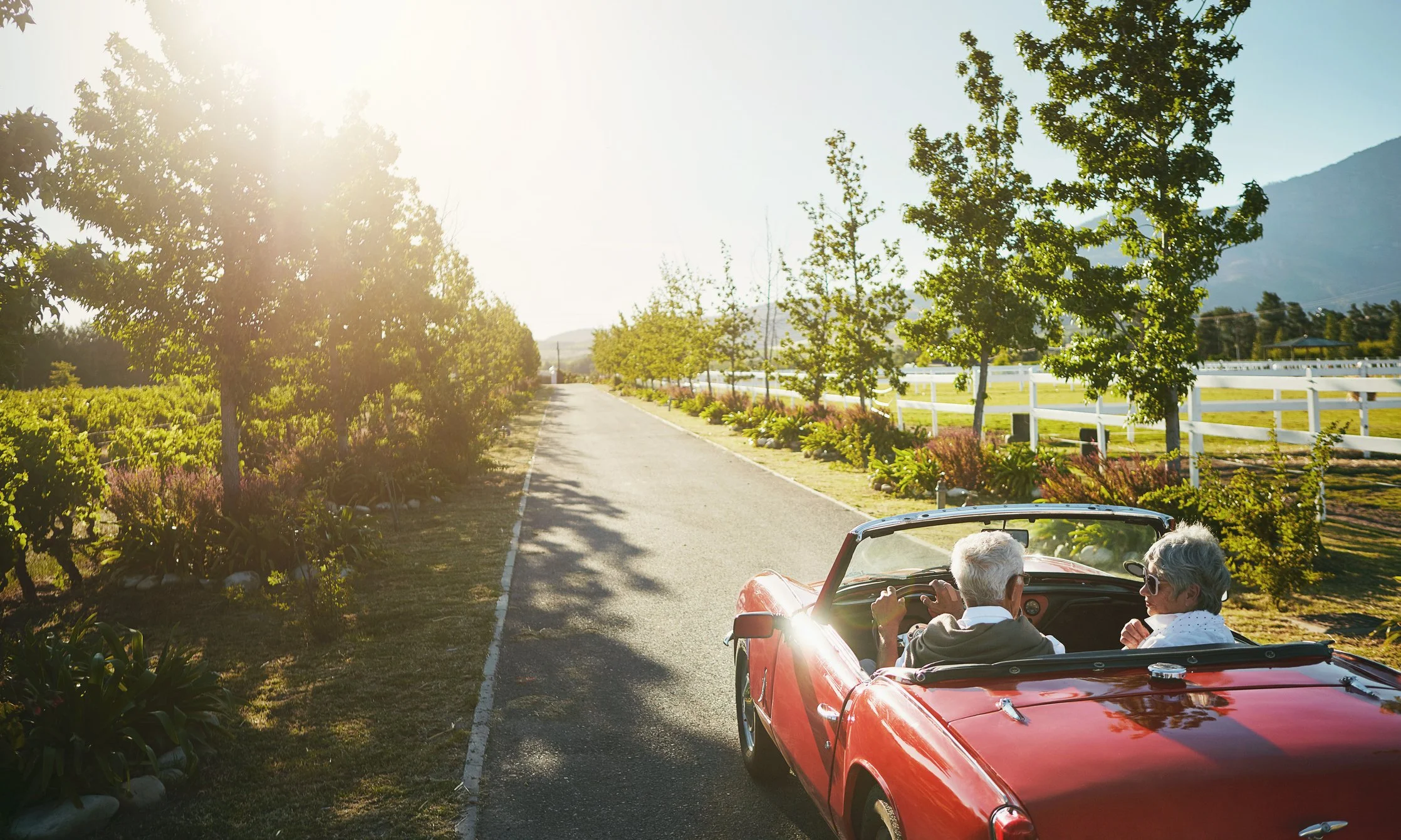 Older couple driving a red convertible down a scenic country road at sunset, representing retirement planning, lifestyle goals, and planning for the future.
