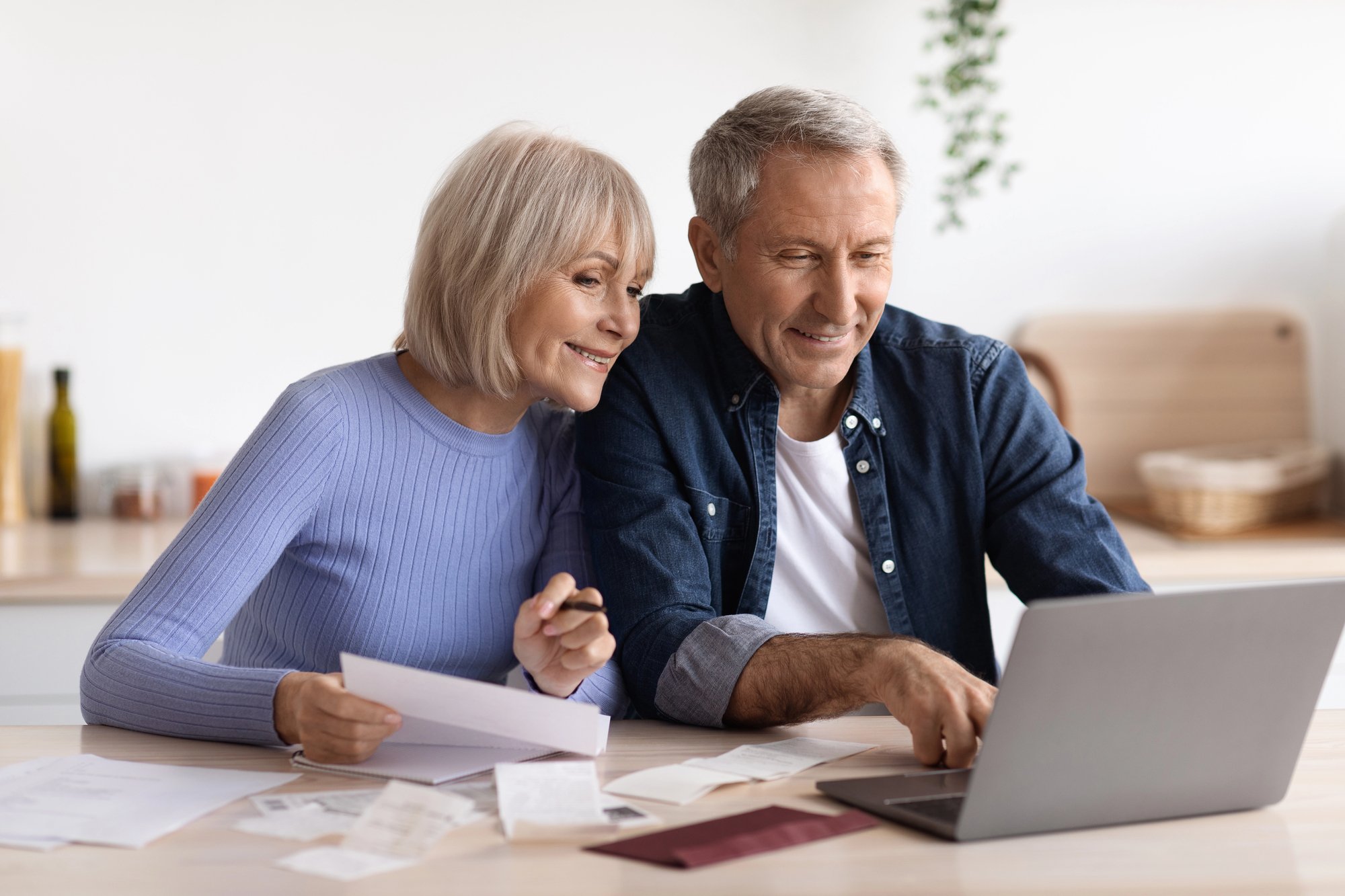 Two older adults reviewing financial documents and using a laptop at home, illustrating retirement tax planning, budgeting, and financial decision-making.