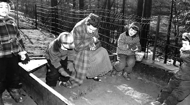 A co-oper listens to children at our old location on New Hampshire Avenue. The playground overlooked Sligo Creek Park. We carried the bits of this sandbox to our new location and used it until it was replaced by our sandpit. We kept two of the boards and the children use these to build slides and platforms.