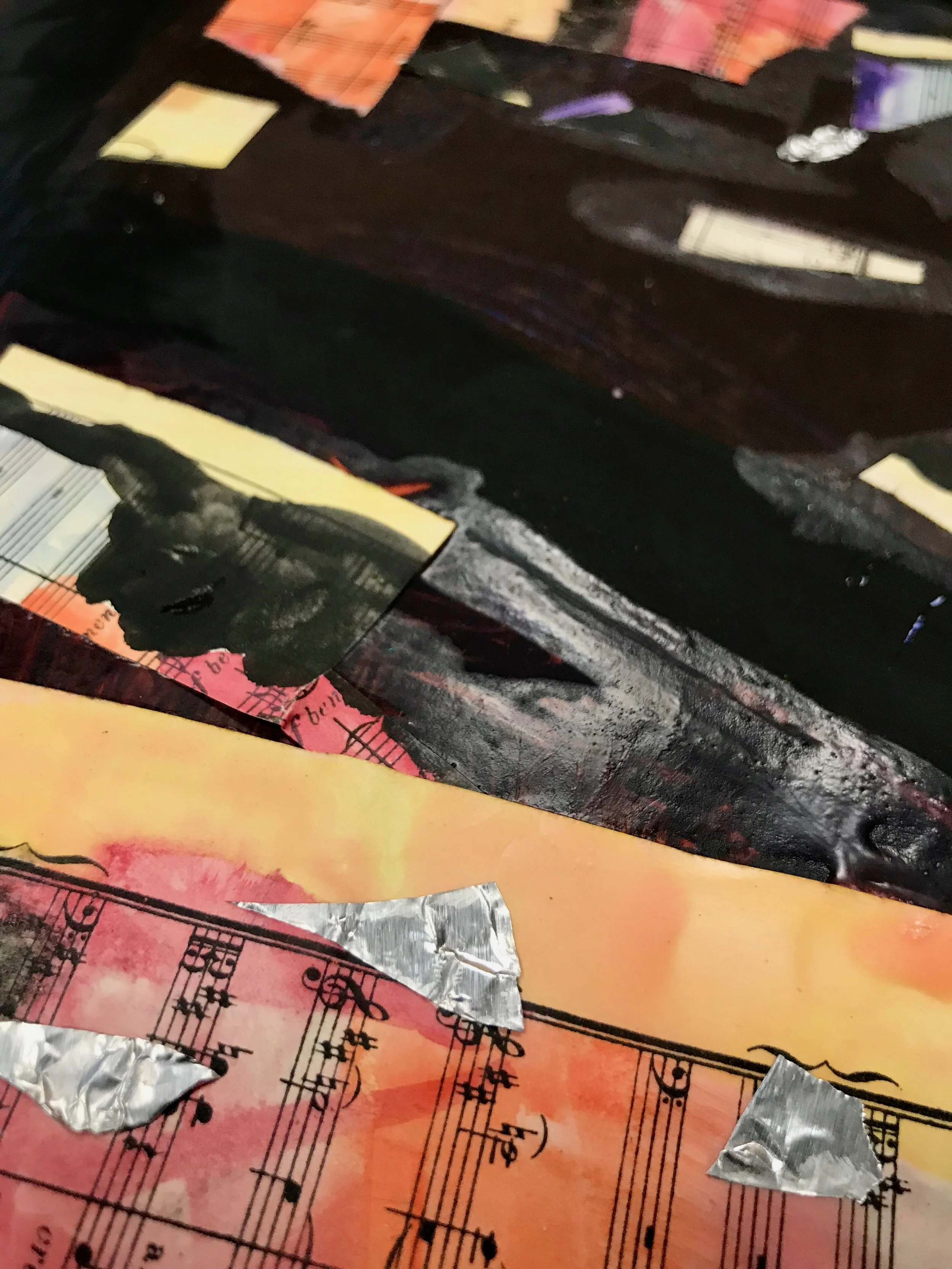 Detail from a child’s work of art. The detail shows the watercolor music sheets cut into smaller rectangle/squares with tin foil embellishments along tempera lines and blocks of color.