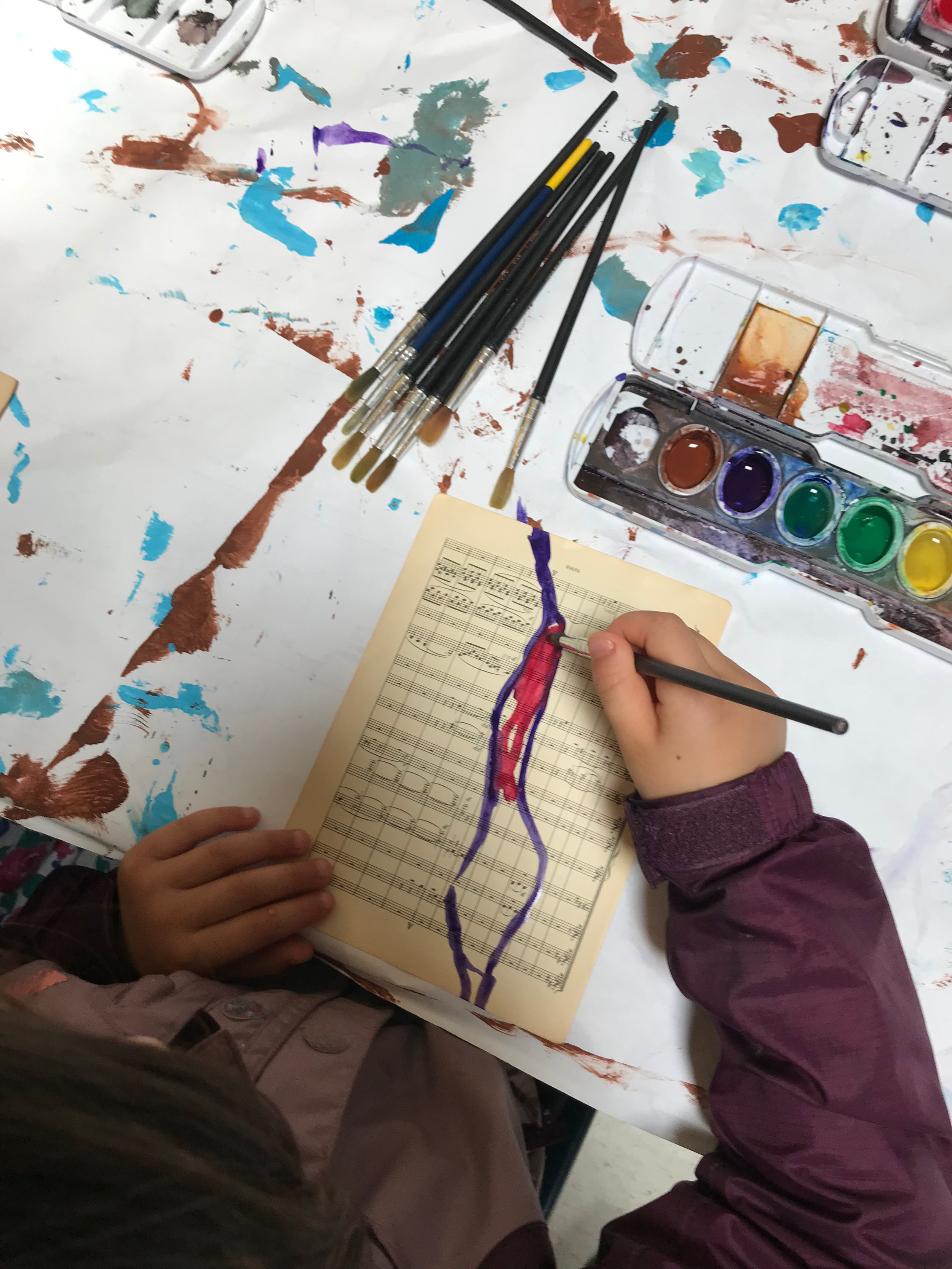 Applying watercolor to a sheet of music. The brush used for the watercolor is a fine brush. It will give both shape and line.