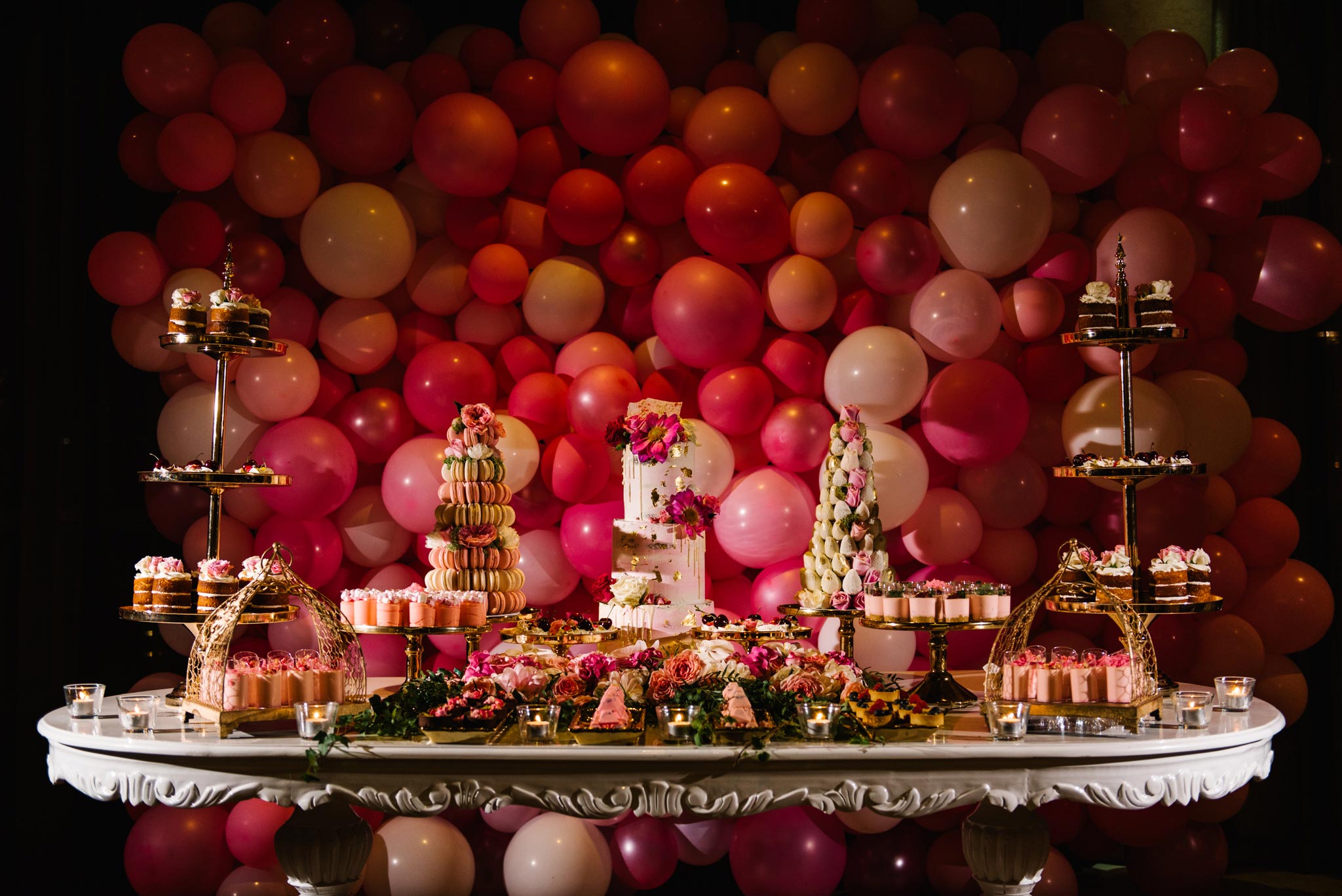 Pink christening cake table with multicolour balloon backdrop